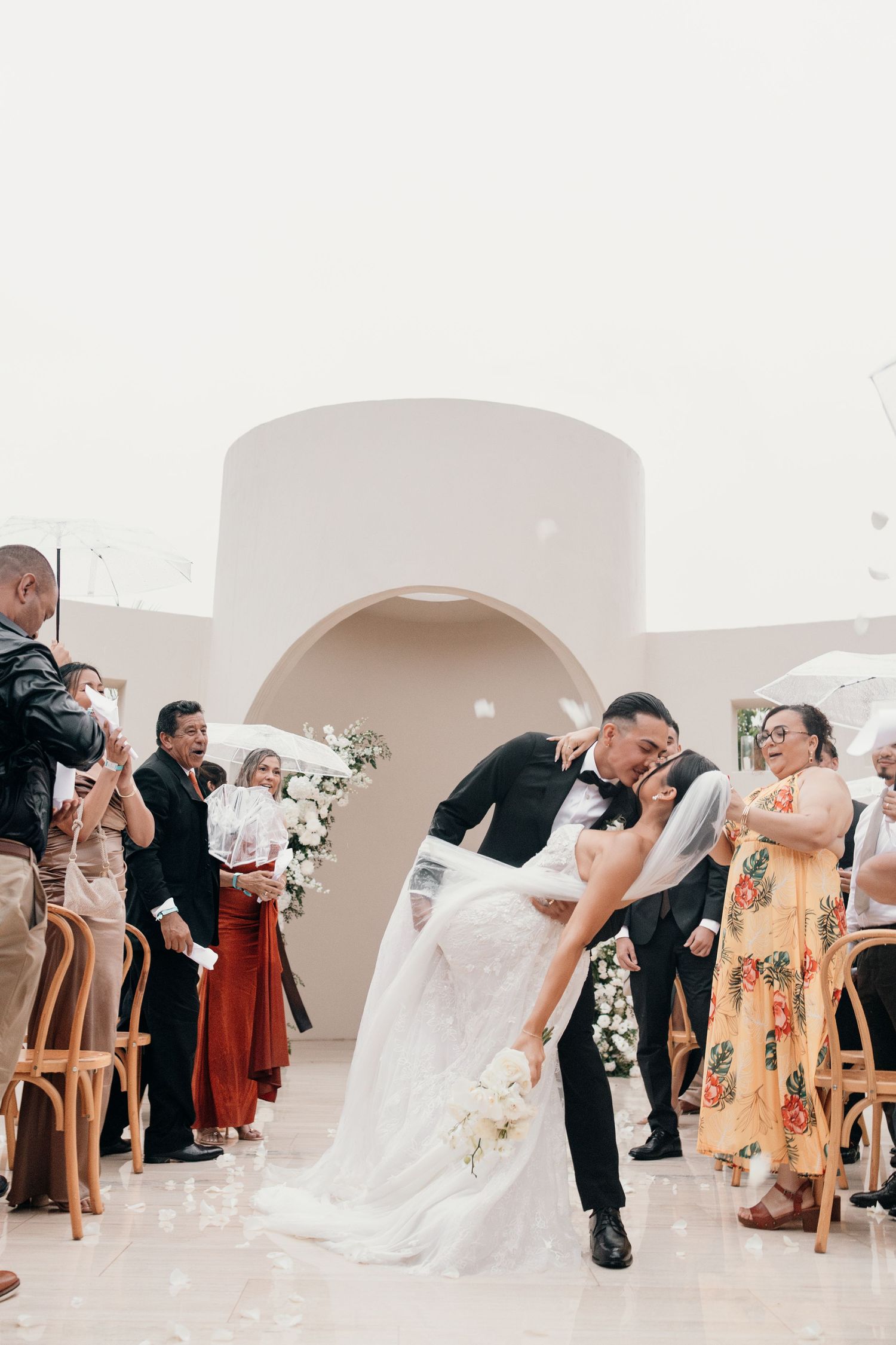 Groom dips bride for a kiss while guests celebrate during an outdoor wedding ceremony recessional.