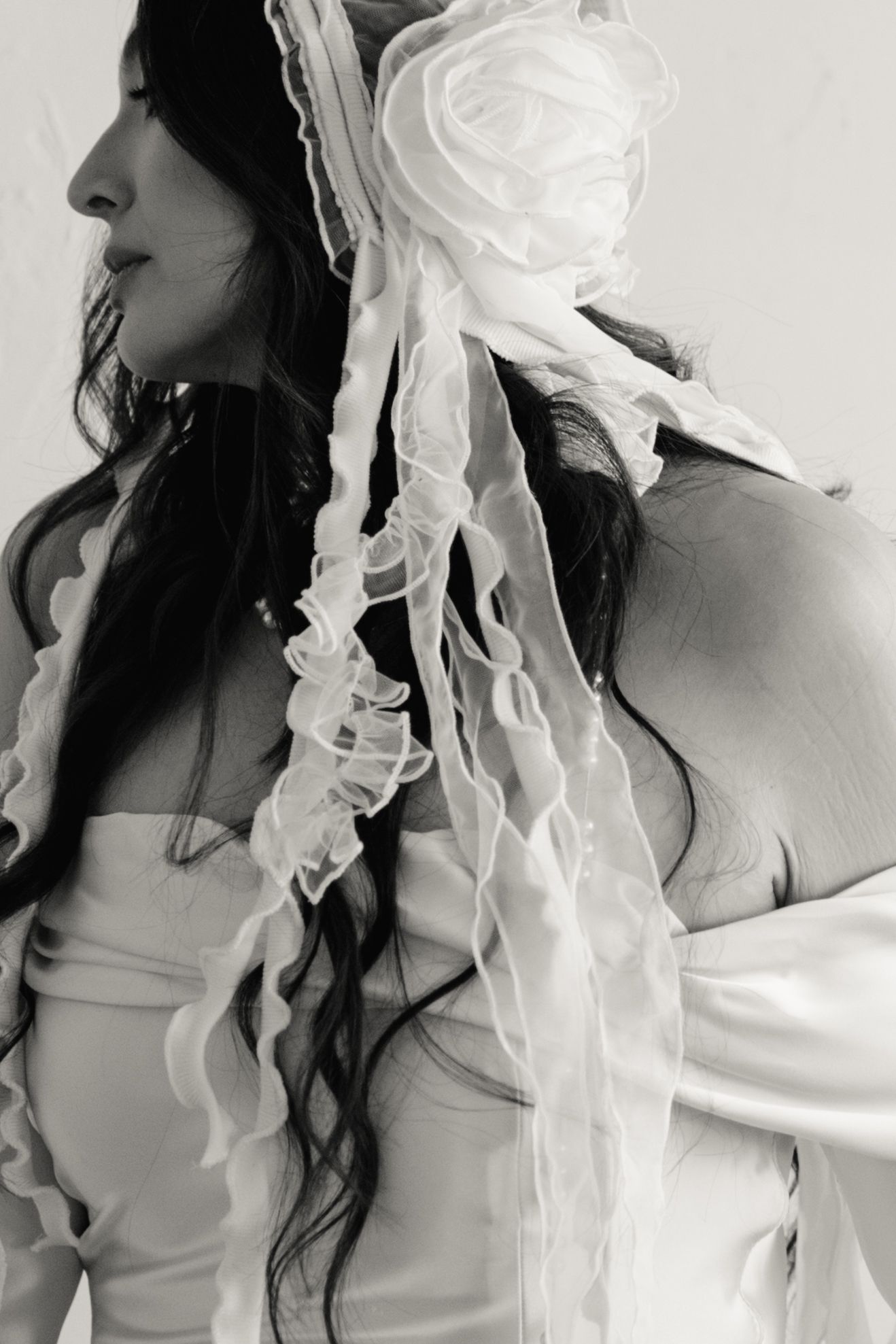 Artistic black and white portrait featuring flowing white veil fabric and dark wavy hair against light background.