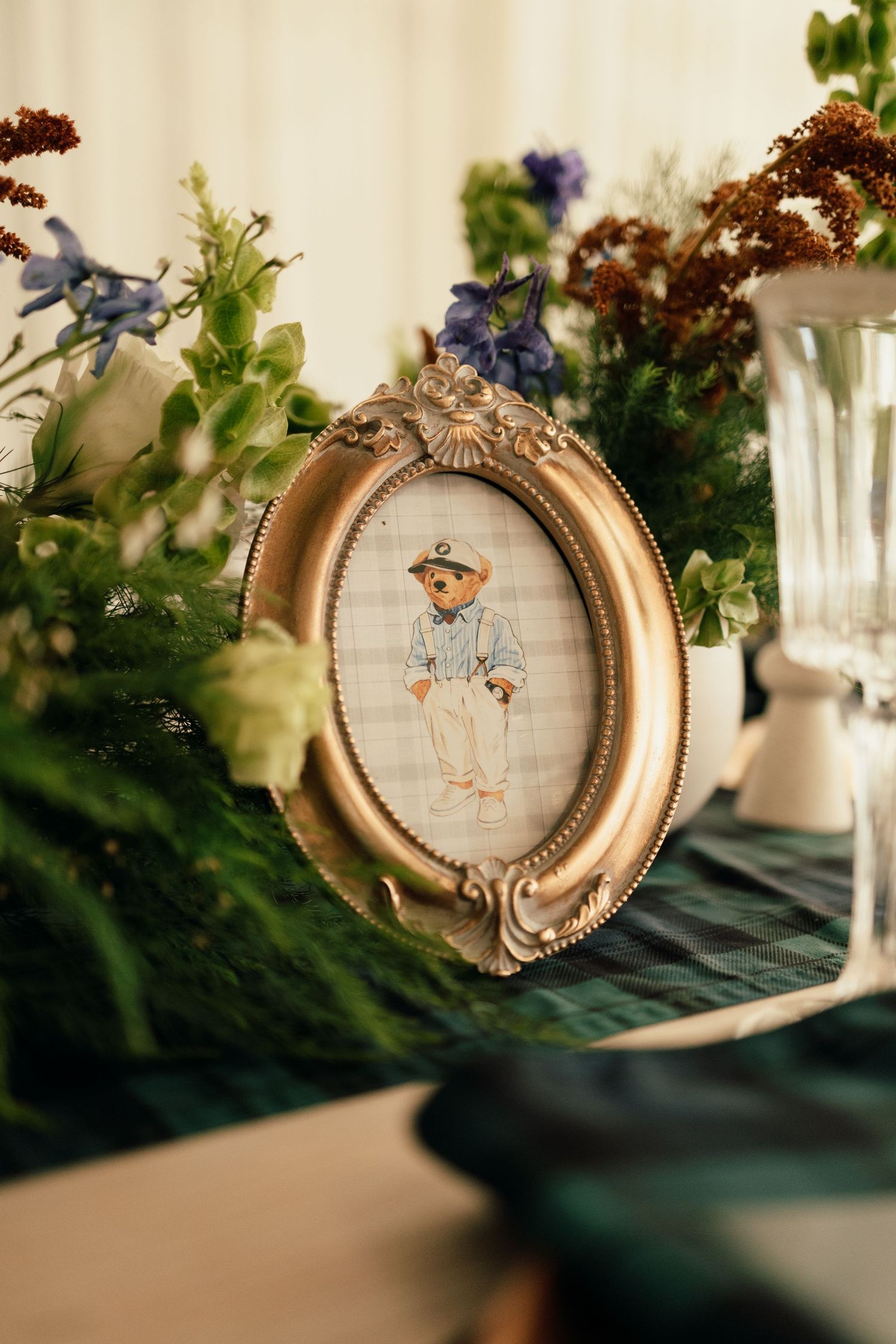 A vintage oval gold frame with embroidered artwork displayed among greenery and floral decorations.