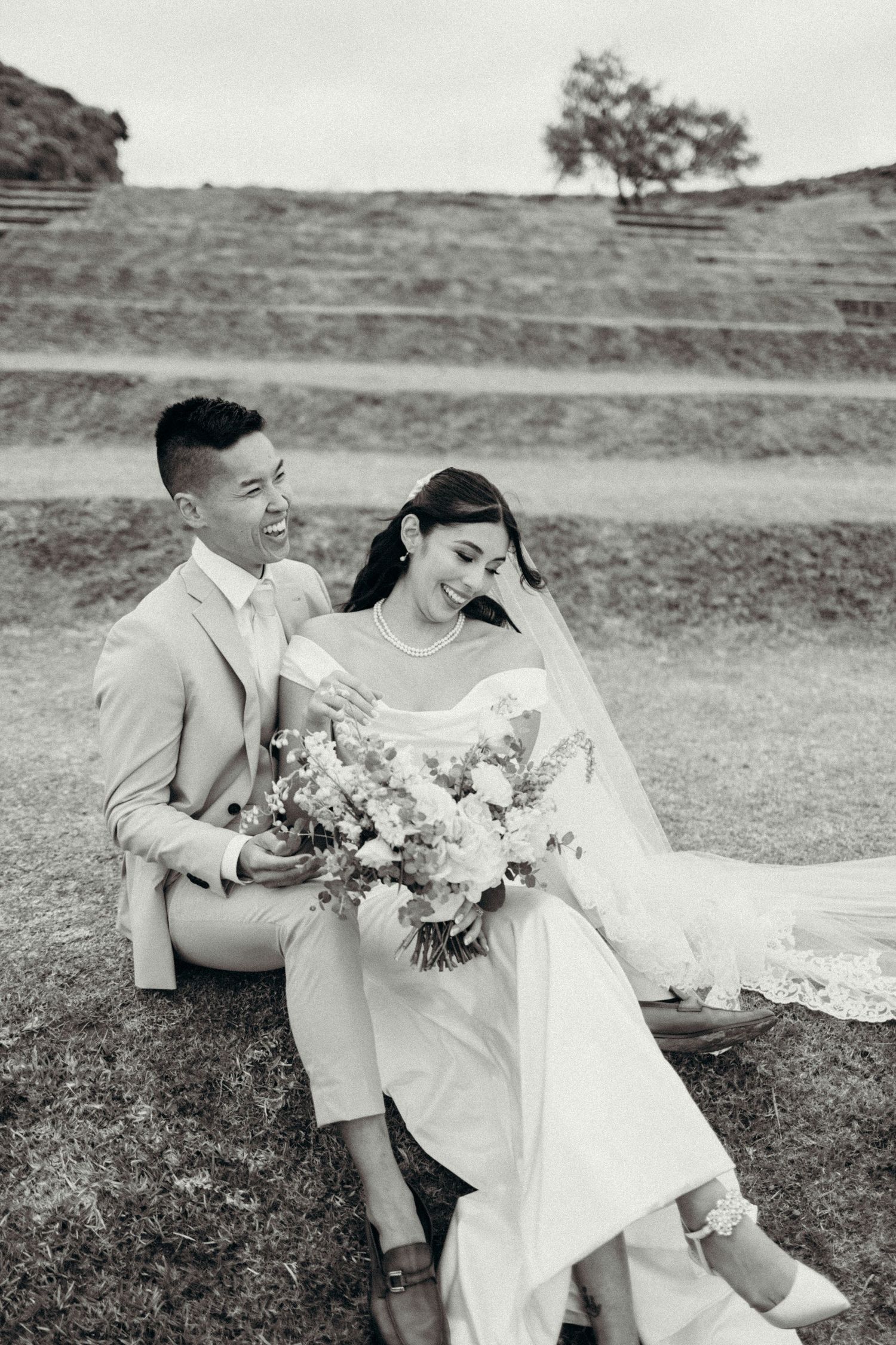 A romantic black and white wedding photo series showing a couple sitting together on grassy hills.