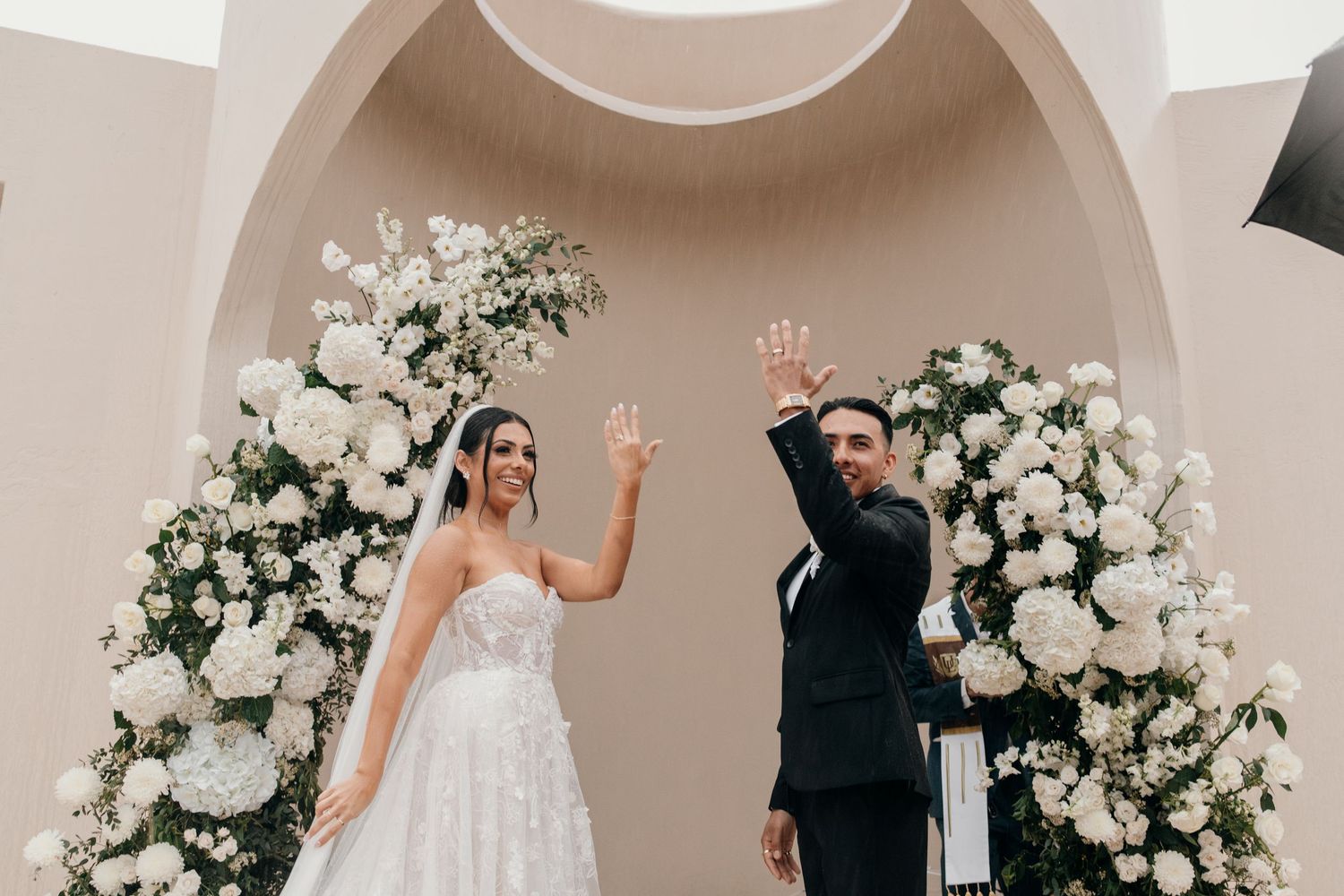 A romantic wedding ceremony takes place in a modern chapel with white floral arrangements and arched windows.