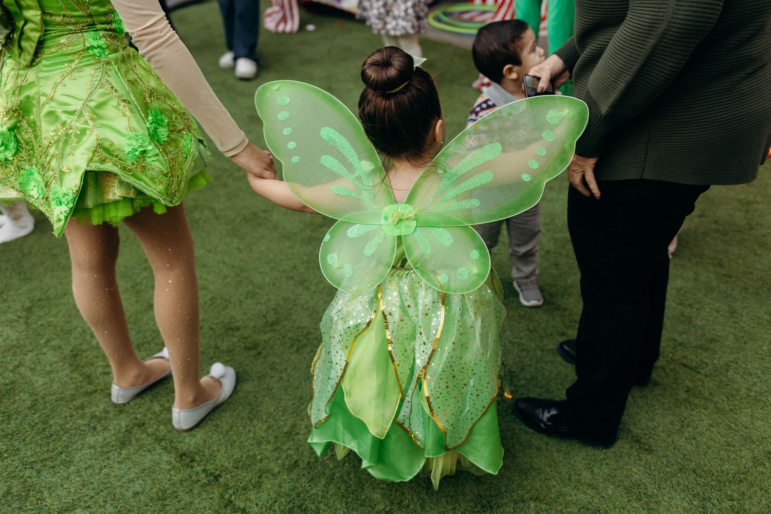 Children in fairy costumes play at an outdoor party with decorative green wings and tulle.