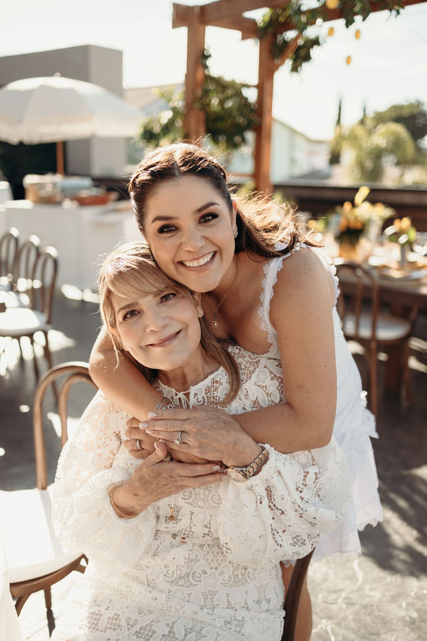 Joyful wedding moment shared between two people in white lace dresses during outdoor reception.