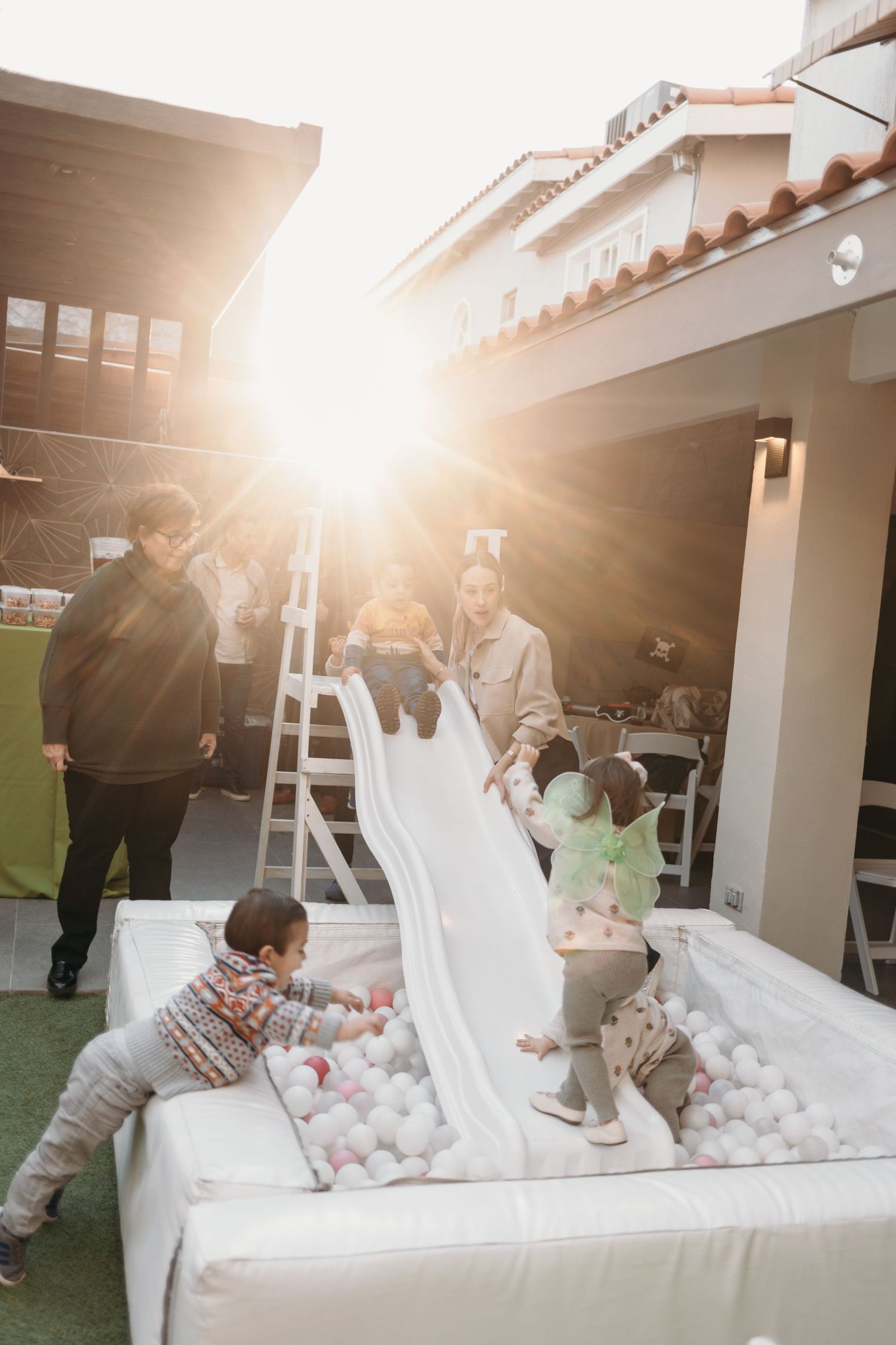 Children play in a white ball pit under bright sunlight at an outdoor party.