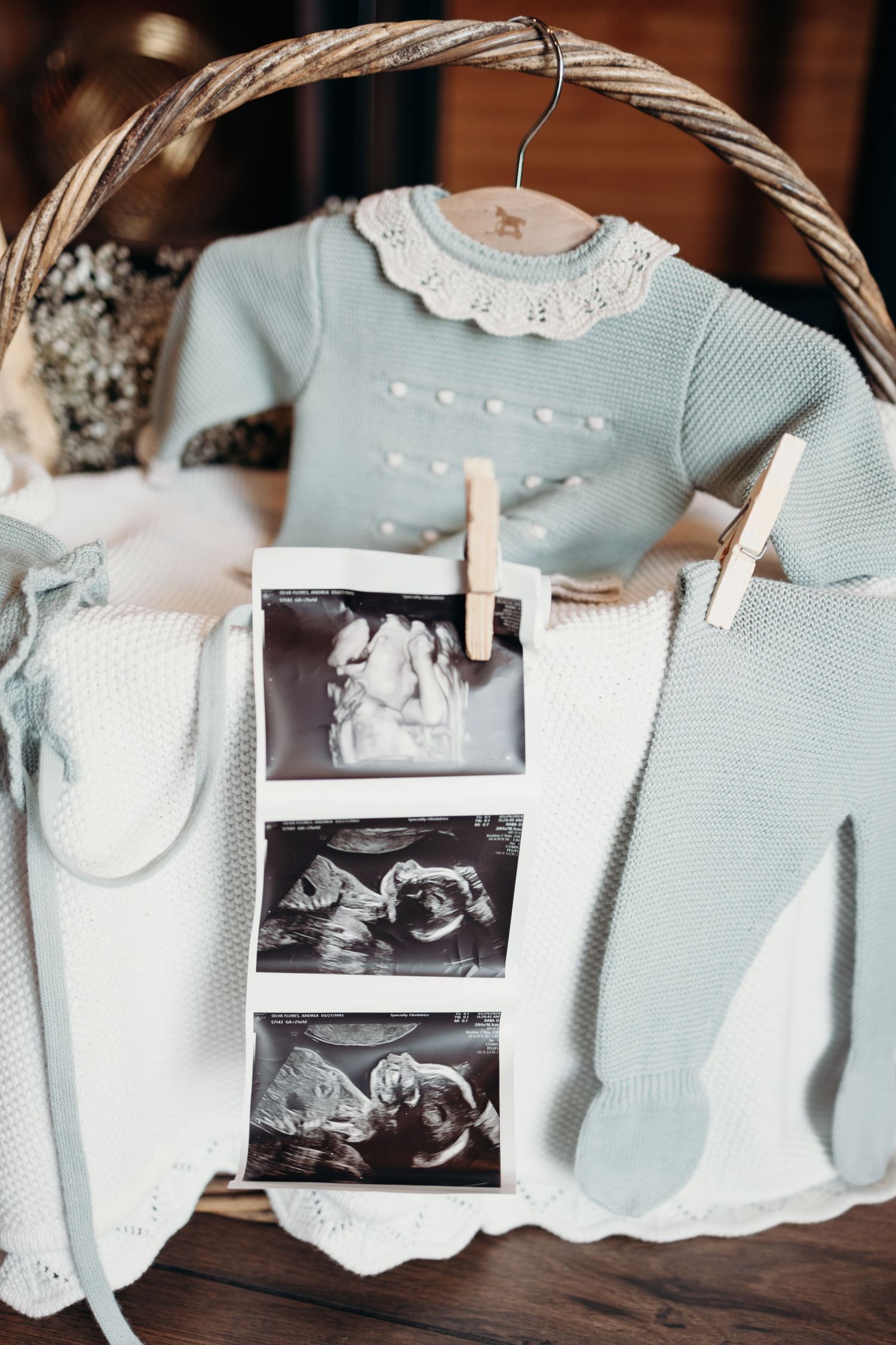 Baby clothes and ultrasound photos displayed in a wicker basket with soft blue outfits.