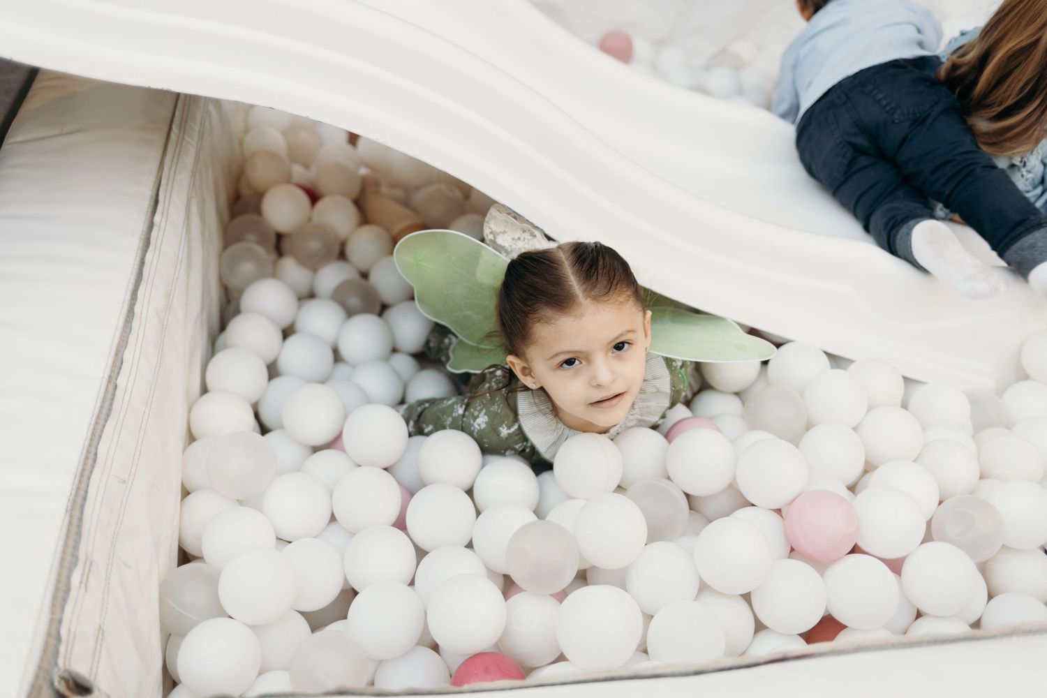 Kids play in a white ball pit filled with pink and white balls at a party.