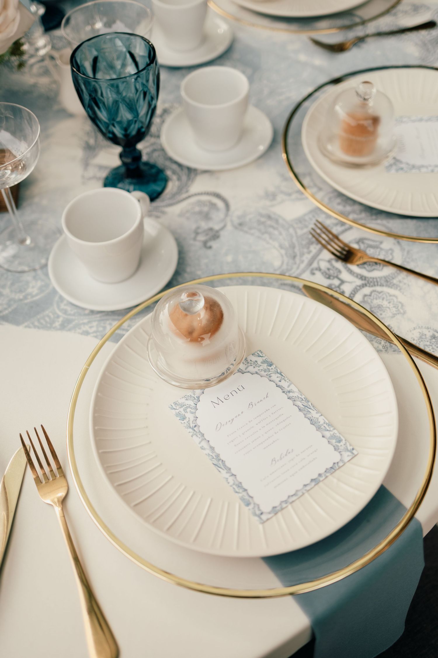 Elegant white plates with gold rims and blue menu cards set on a formal dining table with crystal stemware.