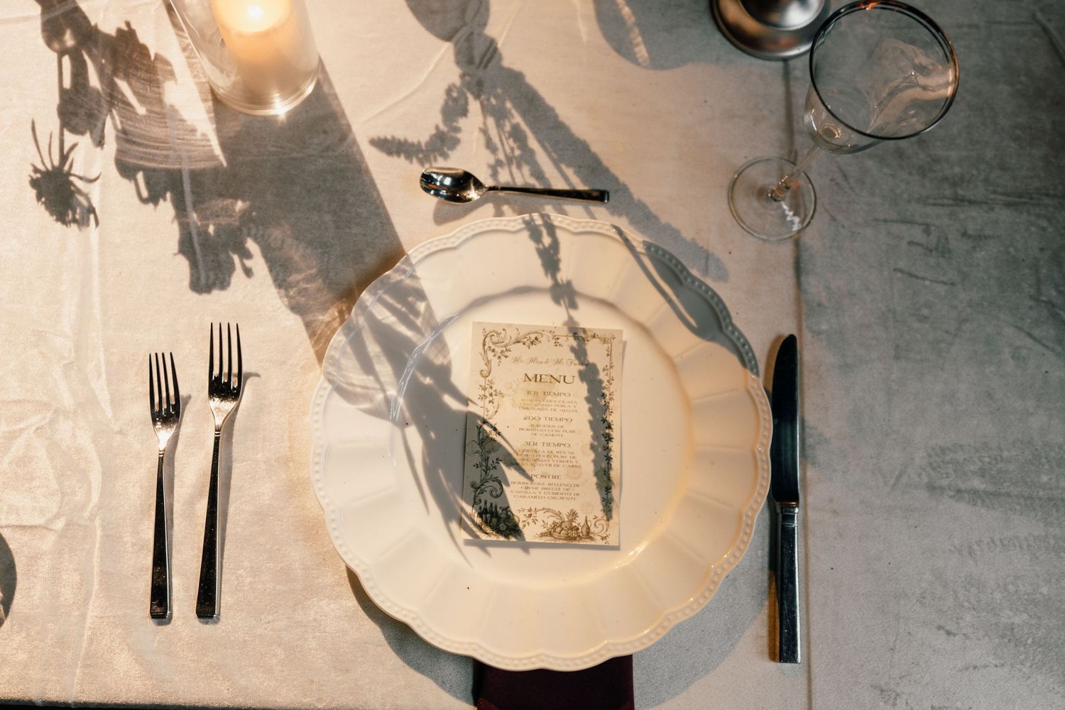 Overhead view of an elegant table setting with white plates, silverware and wine glasses in natural light.