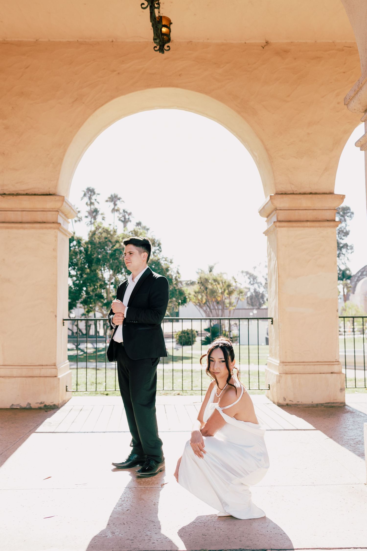 A wedding couple poses creatively under arched columns with dramatic lighting and shadows.