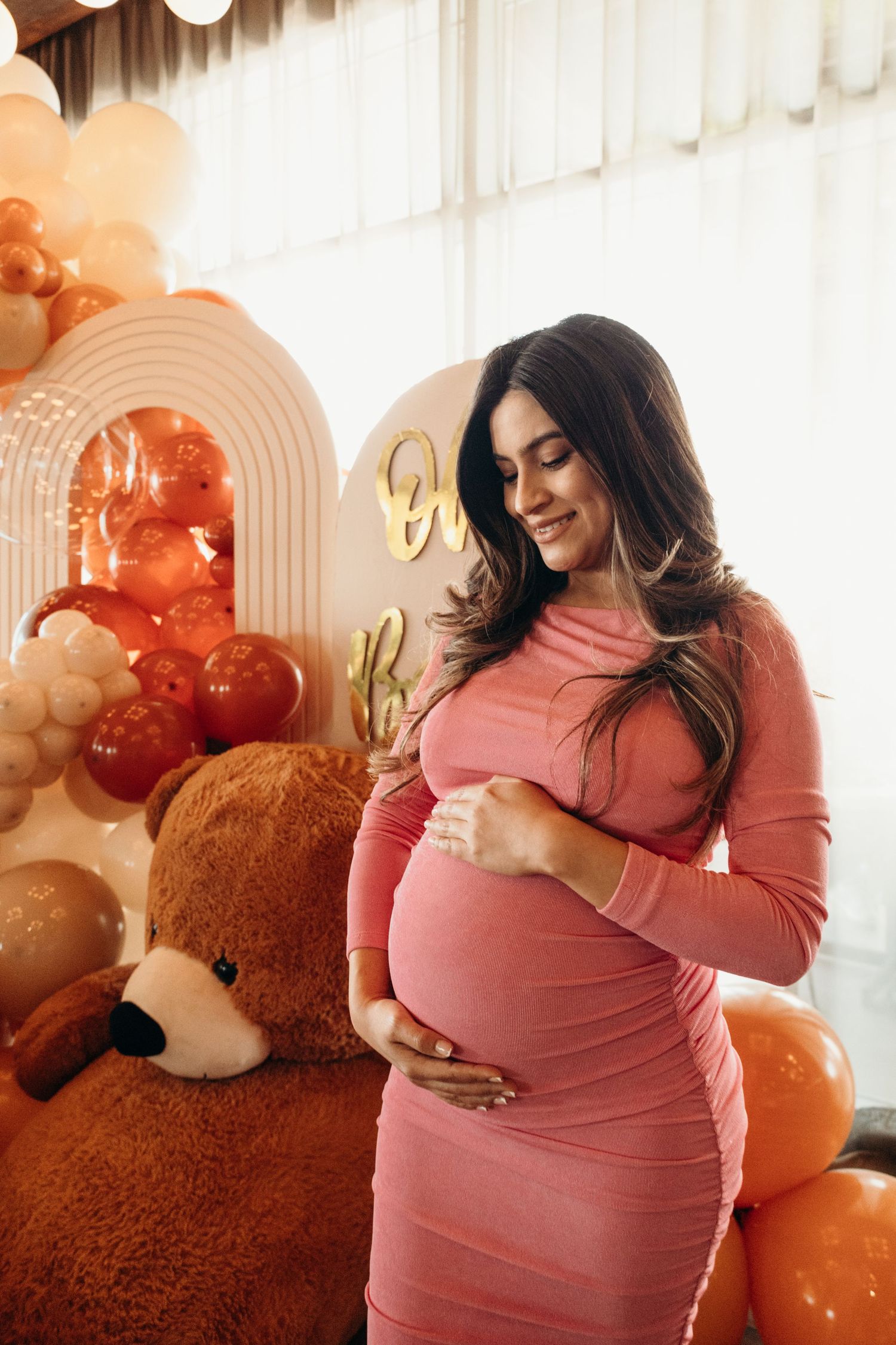 Expectant mother in coral dress poses with balloons during pregnancy photoshoot.