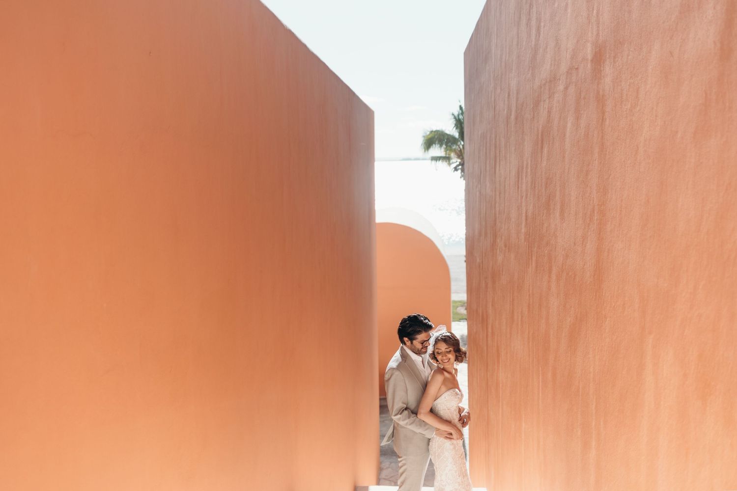 Couple embraces between terracotta walls in a romantic outdoor wedding portrait.