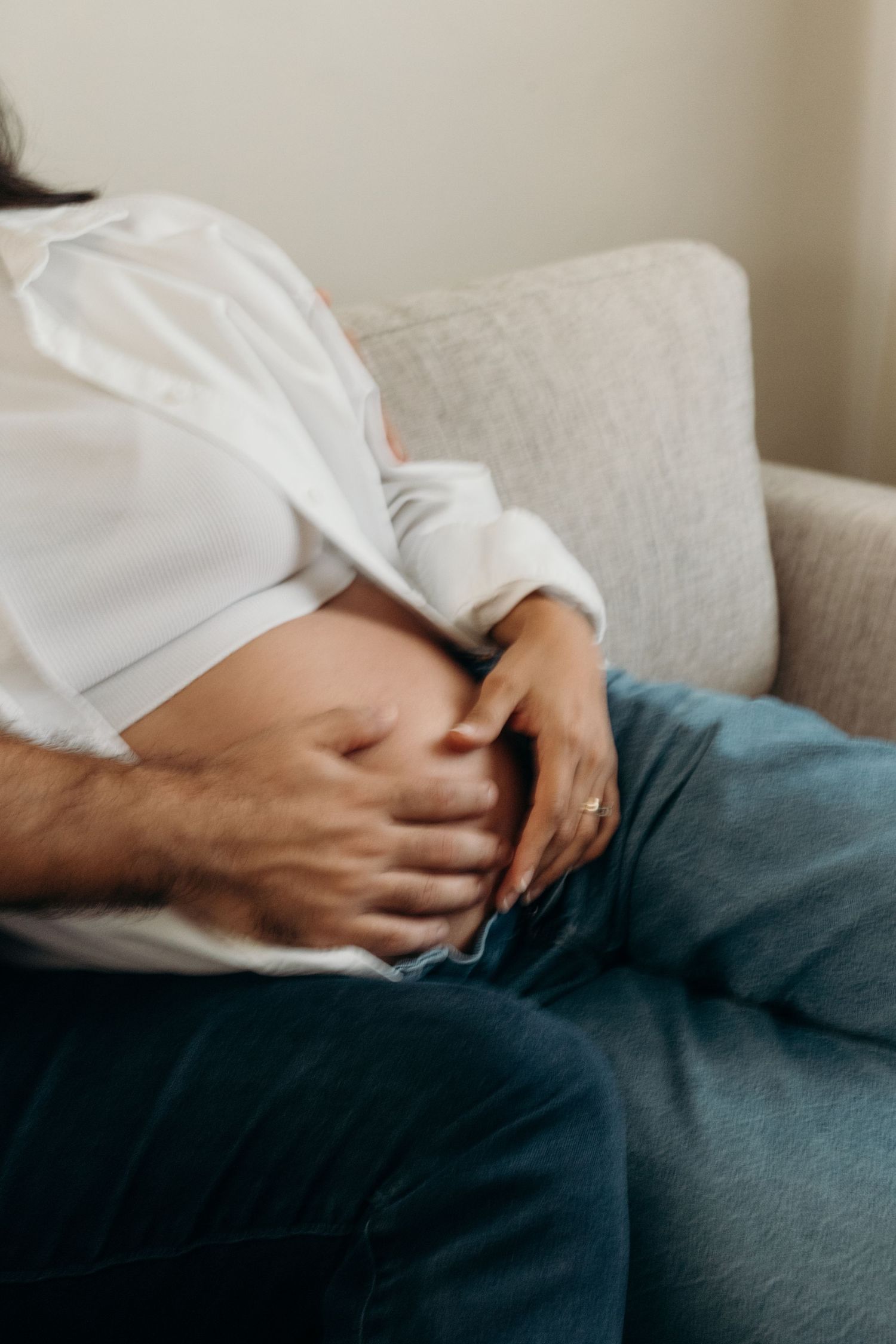 Close-up view of hands resting on a dark couch showing intimate moments during pregnancy.