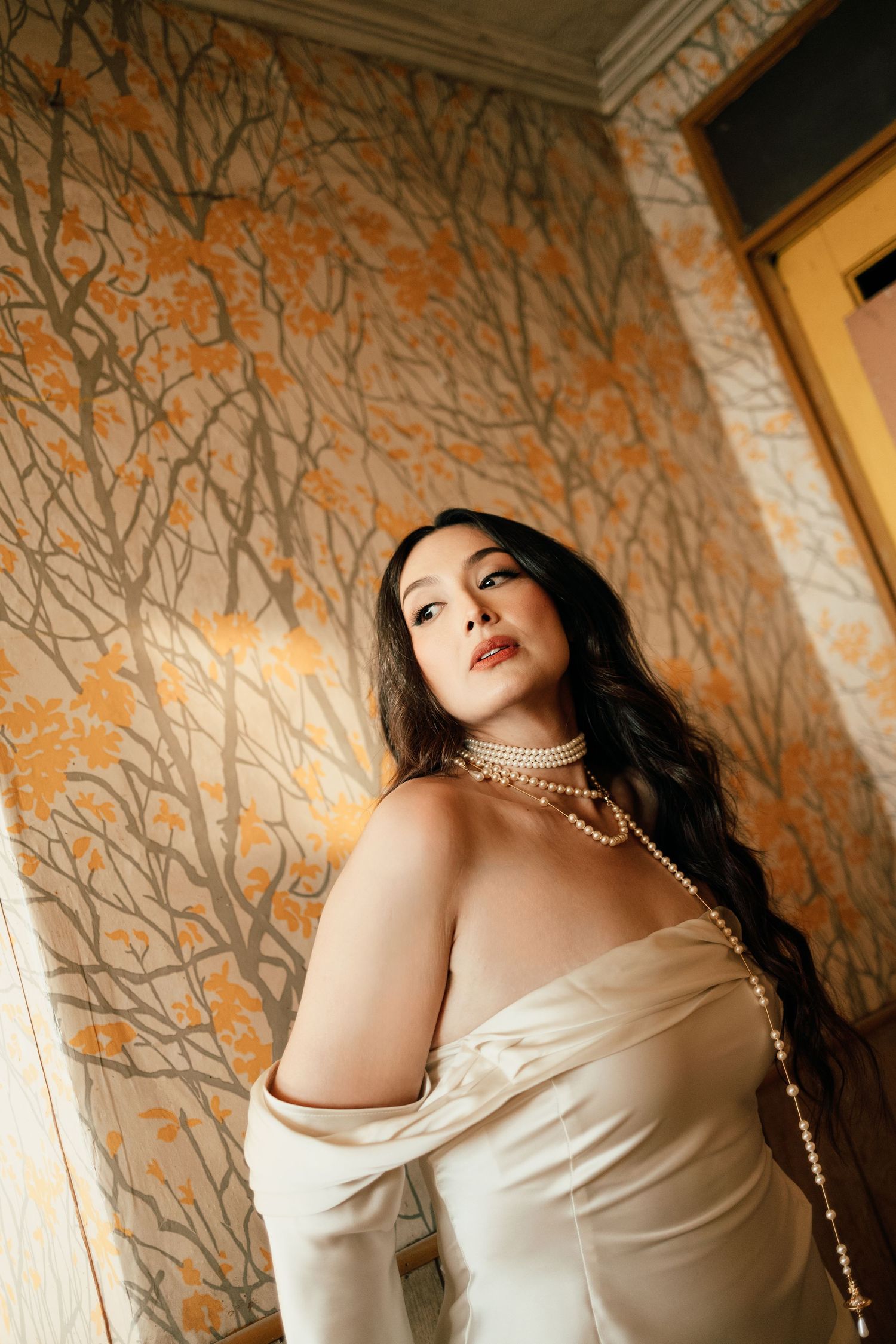 Artistic boudoir photo series showing off-shoulder white satin dress against textured golden wallpaper in warm lighting.