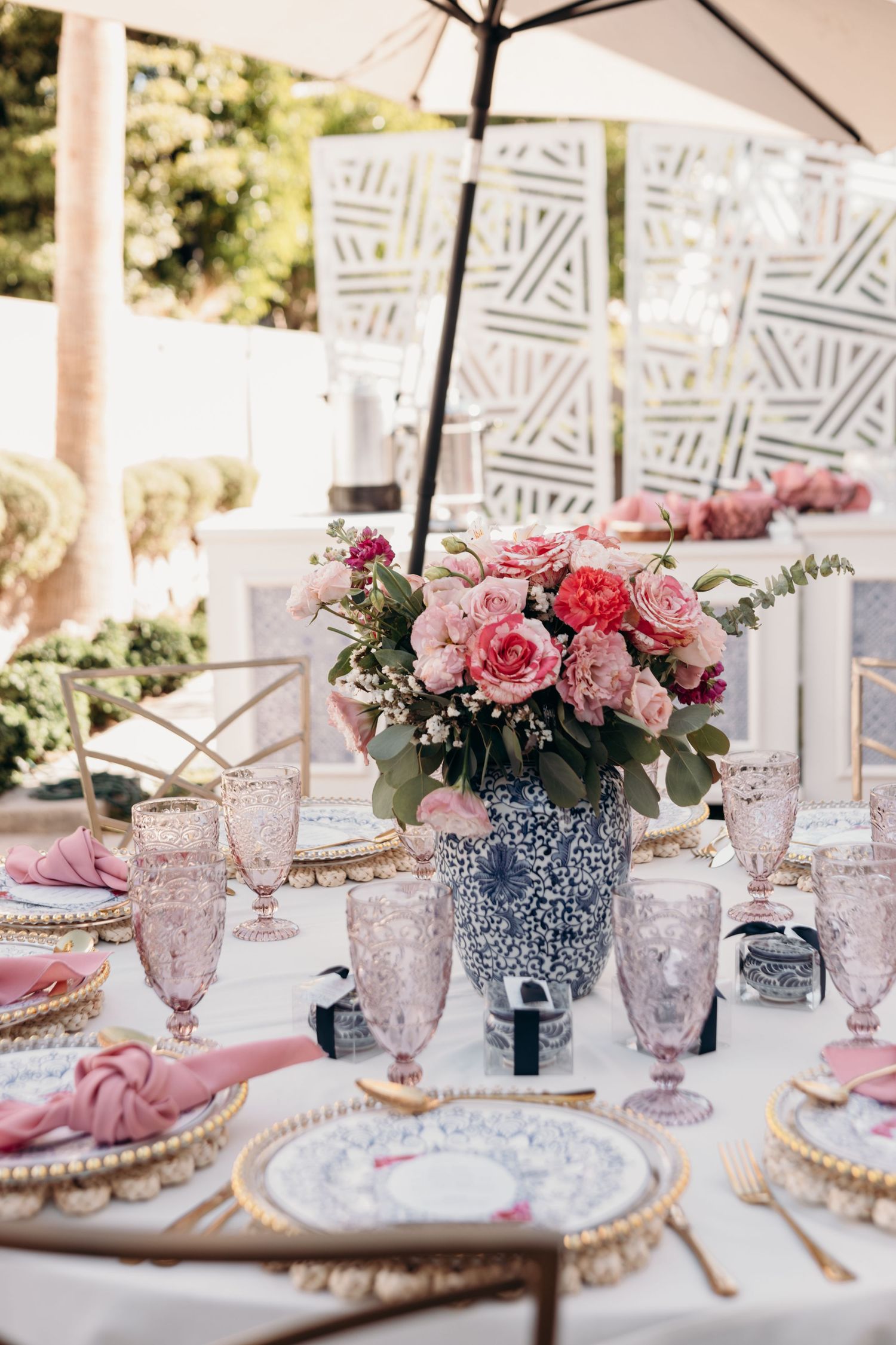 Elegant outdoor table setting with pink flowers in blue and white vases and crystal stemware.