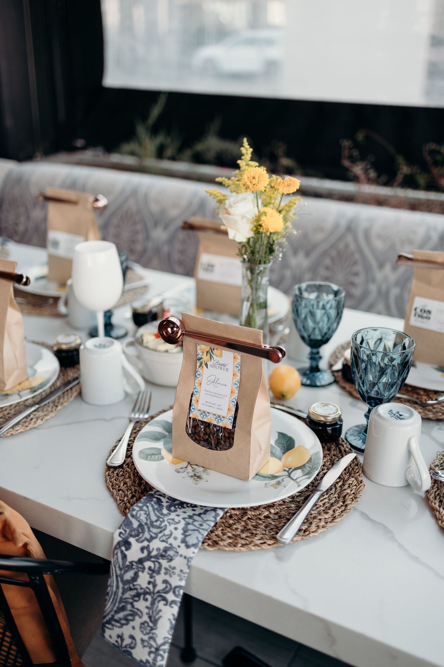 Rustic wedding table setting with blue glassware, kraft paper name cards, and delicate floral accents.