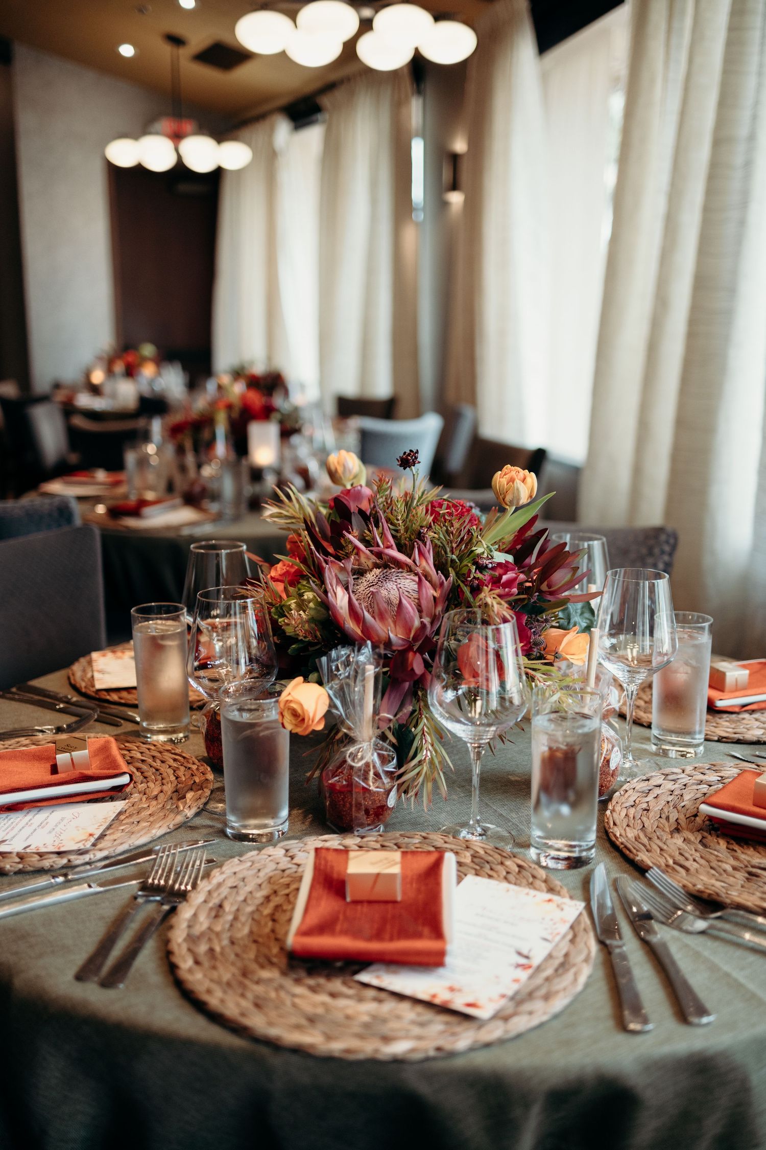 Formal table setting with protea centerpiece, woven chargers, and crystal glassware at wedding reception.