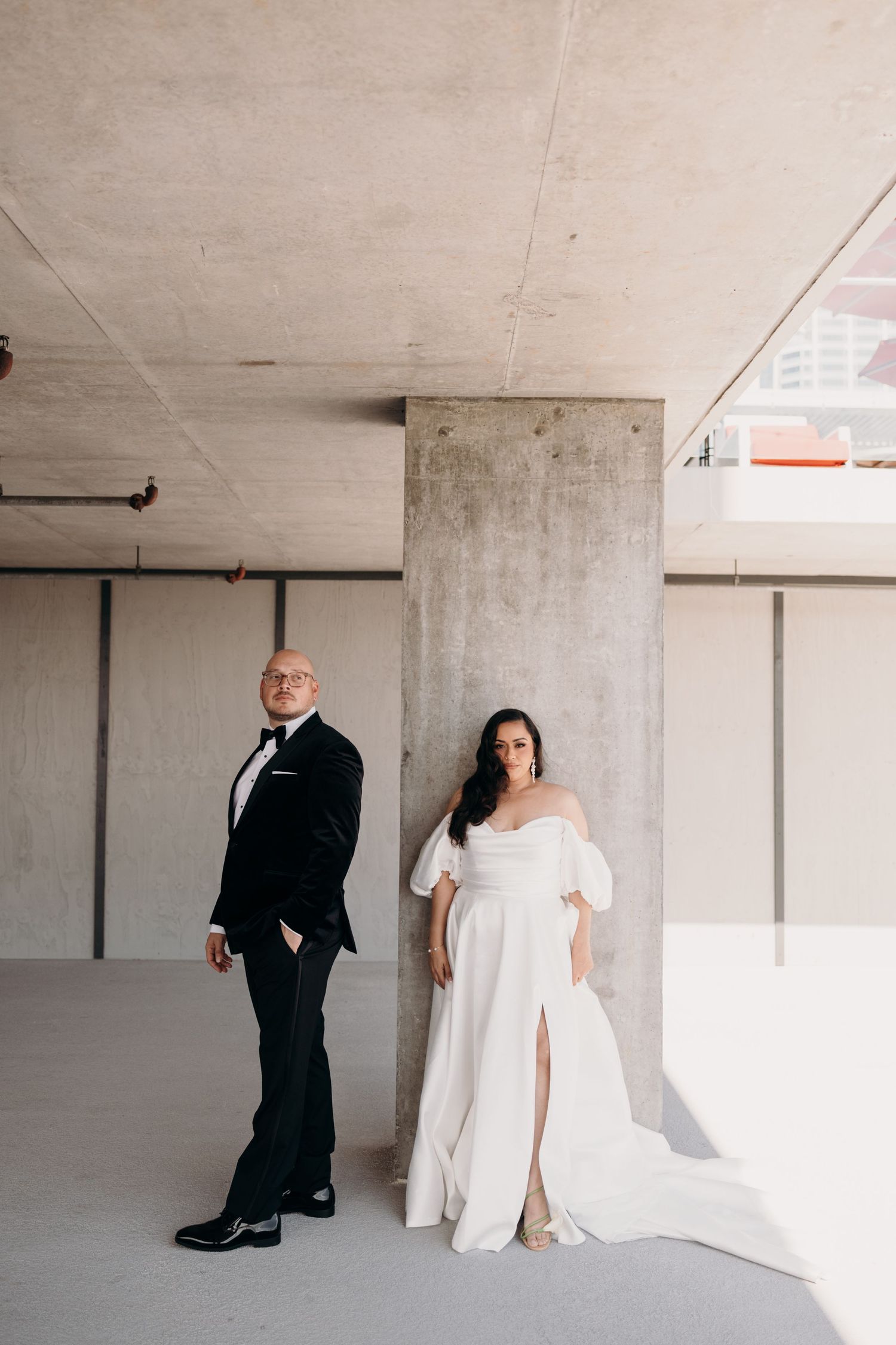 Modern wedding couple poses in an industrial parking garage with concrete pillars and minimalist aesthetic.