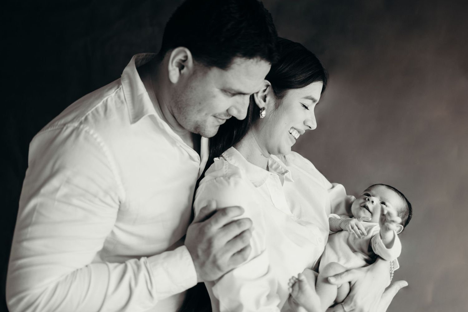 Black and white photo series showing tender family moments with a newborn baby in an intimate home setting.