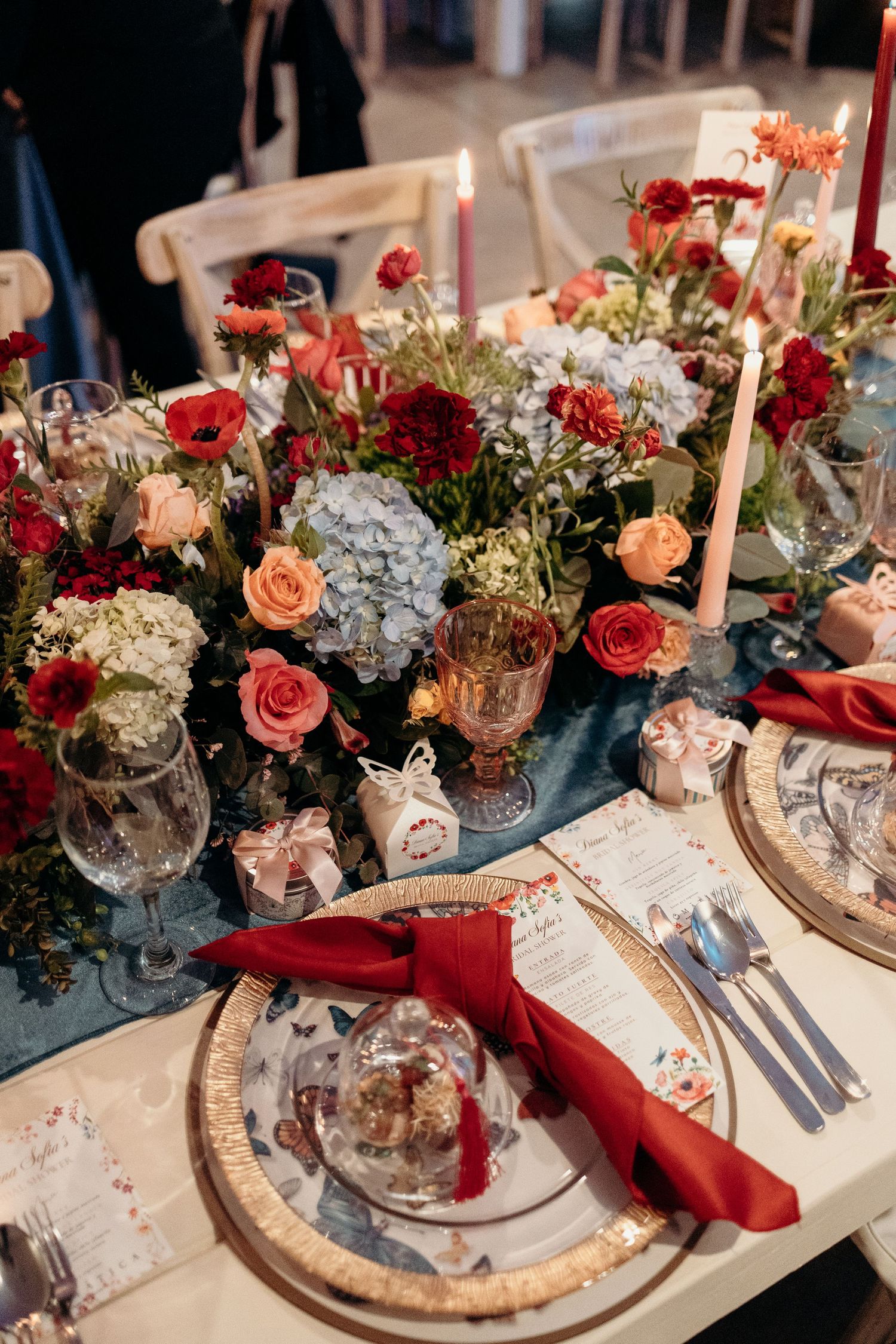 Elegant table setting with red and pink flowers, crystal candleholders, and vintage-inspired place settings.