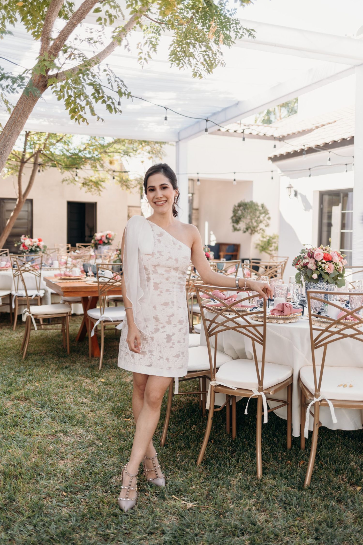 Outdoor wedding reception setup with white tent, wooden chairs and tables decorated with floral arrangements.