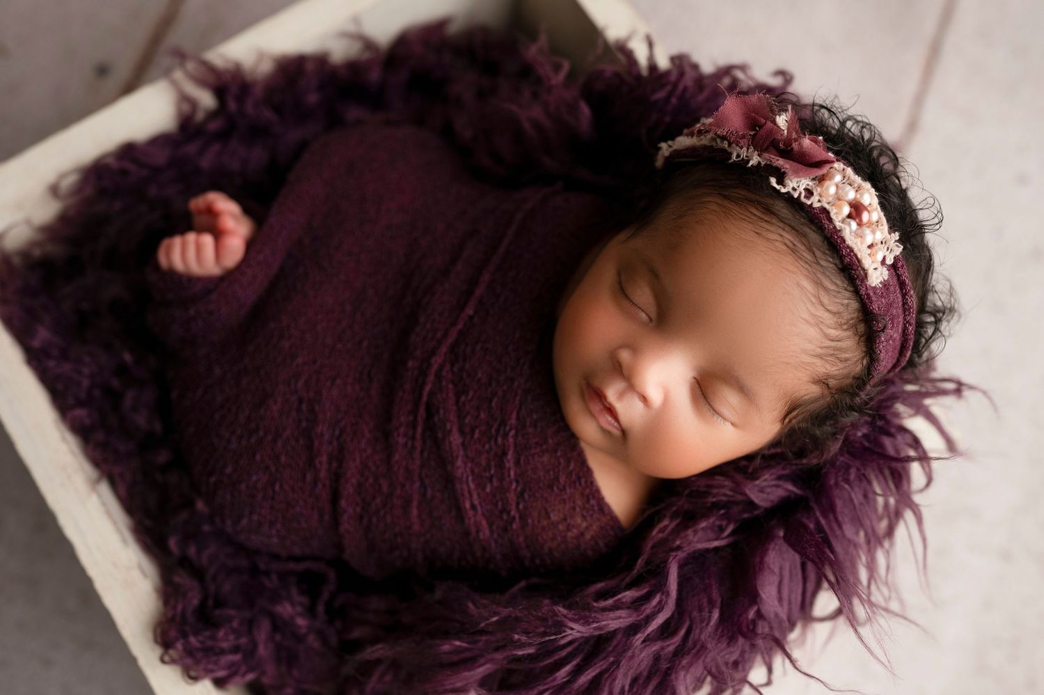 A person with curly purple hair lies on dark fabric in a creative portrait series.