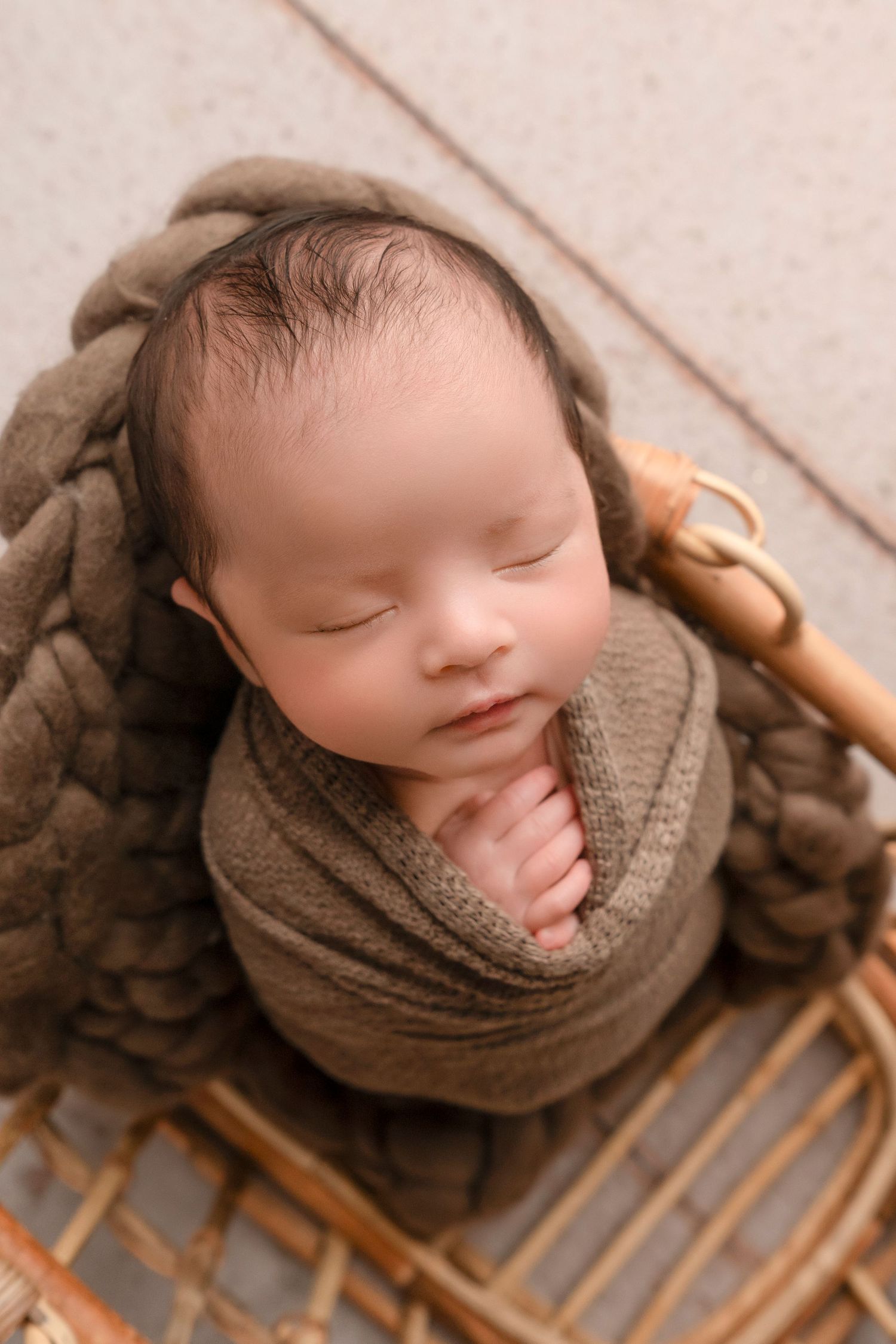 Sleeping newborn wrapped in brown knit blanket resting on wooden sled prop in studio setting.