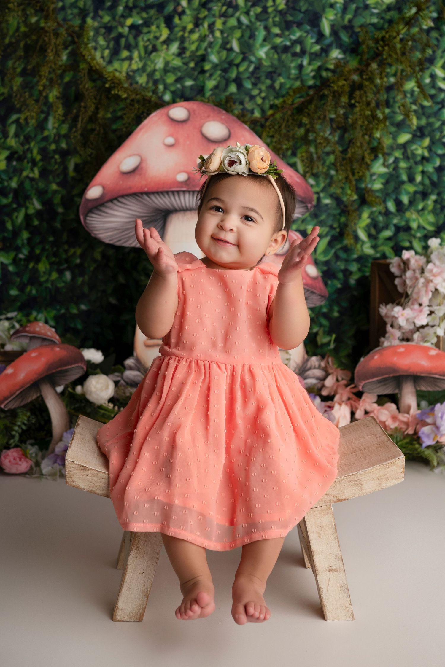 Adorable toadstool-themed photo session with pink dress and mushroom decorations against a leafy backdrop.