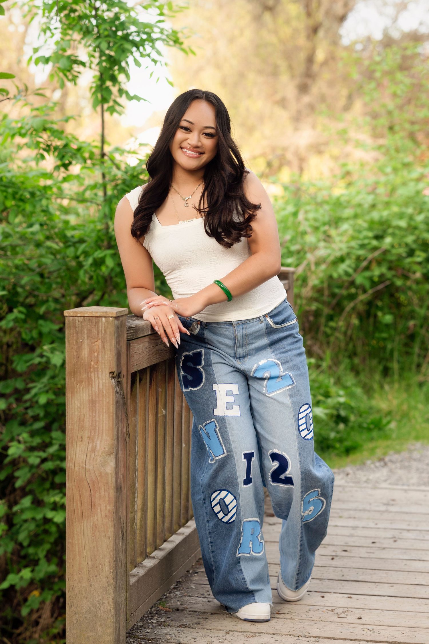 Person wearing customized denim jeans with patches and numbers poses on wooden boardwalk surrounded by greenery.