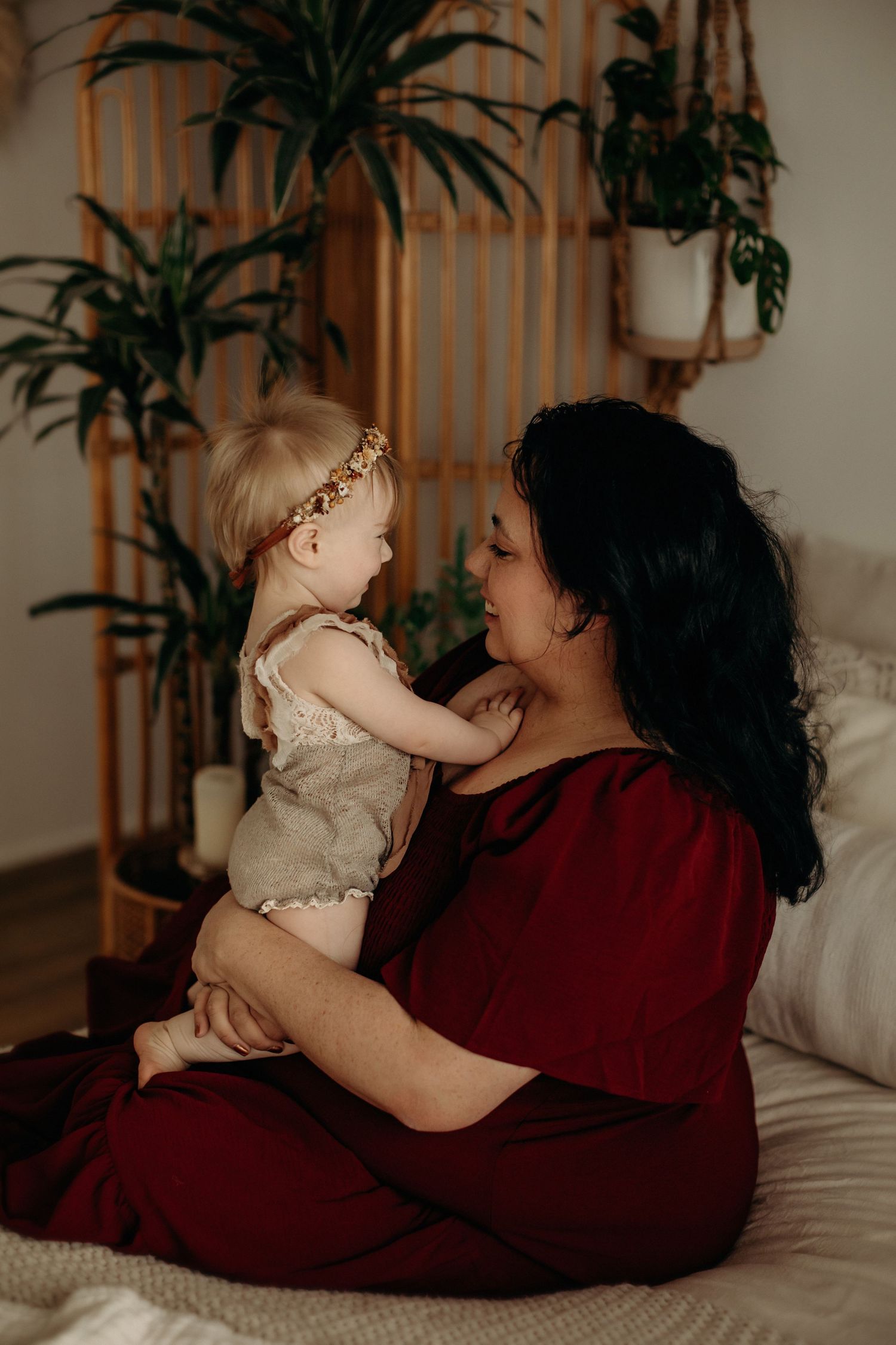 Intimate lifestyle photography of mother and baby sharing tender moments on bed with houseplants.