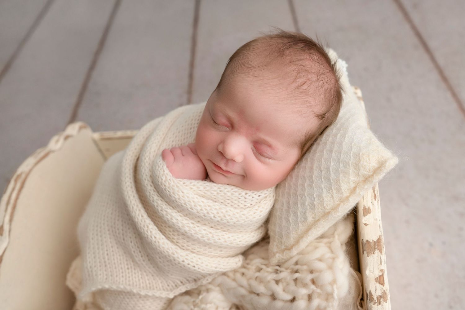 Sleeping newborn wrapped in soft cream-colored blanket resting peacefully in wooden basket.