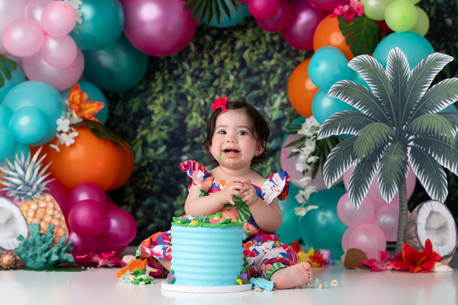Colorful balloon arch with tropical decorations featuring palm leaves and vibrant flowers for a festive party setup.
