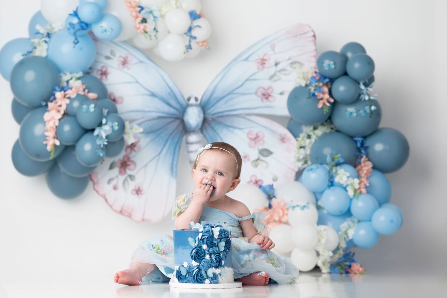 Festive party setup with blue balloons, butterflies and a small blue cake for a baby celebration.