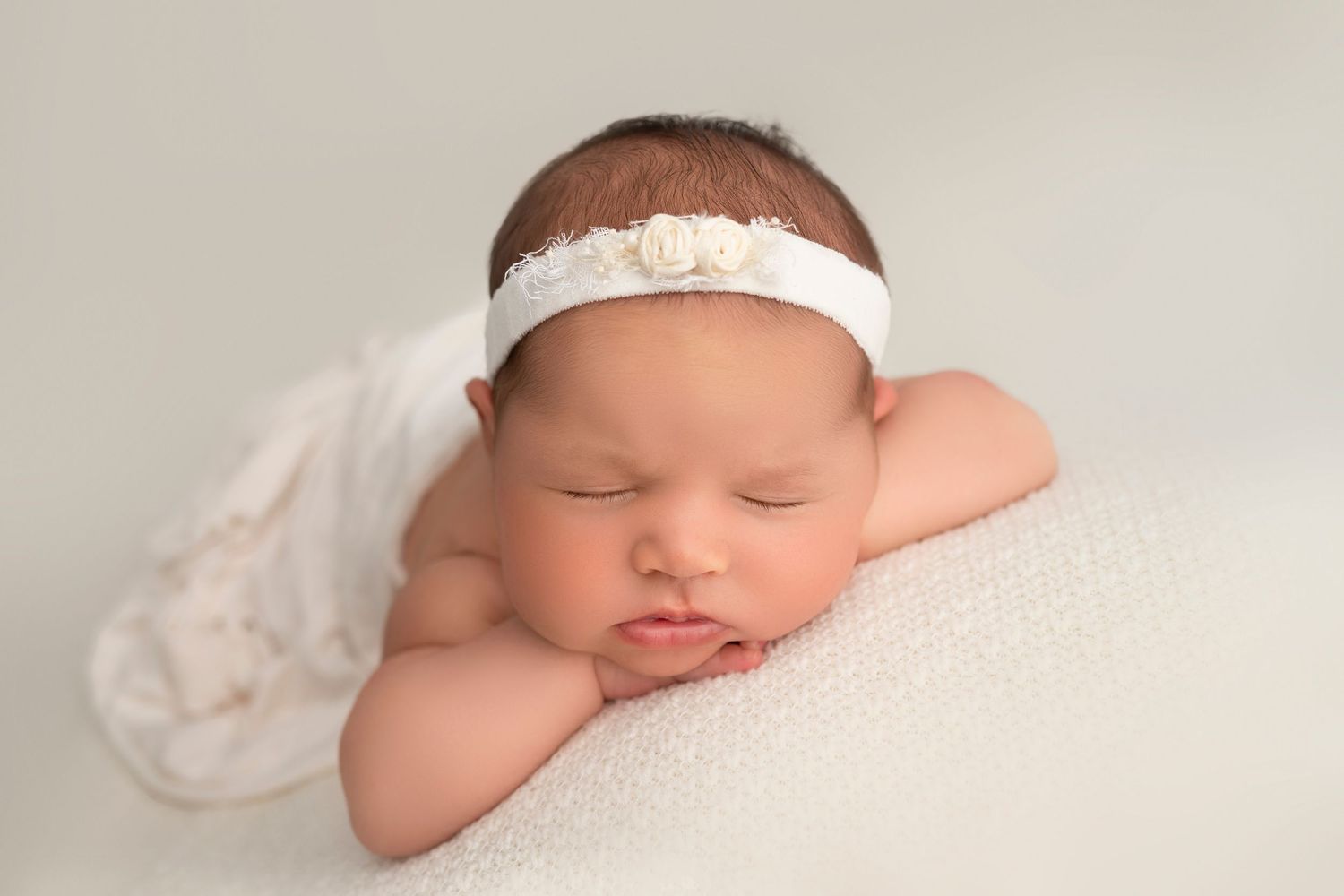 Newborn baby sleeping peacefully on soft white blanket wearing a delicate lace headband.