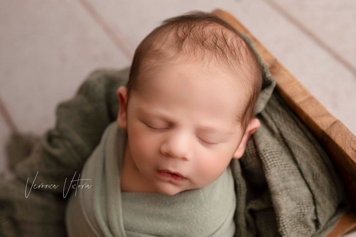 Artistic newborn portraits featuring a baby swaddled in sage green fabric on a wooden surface.