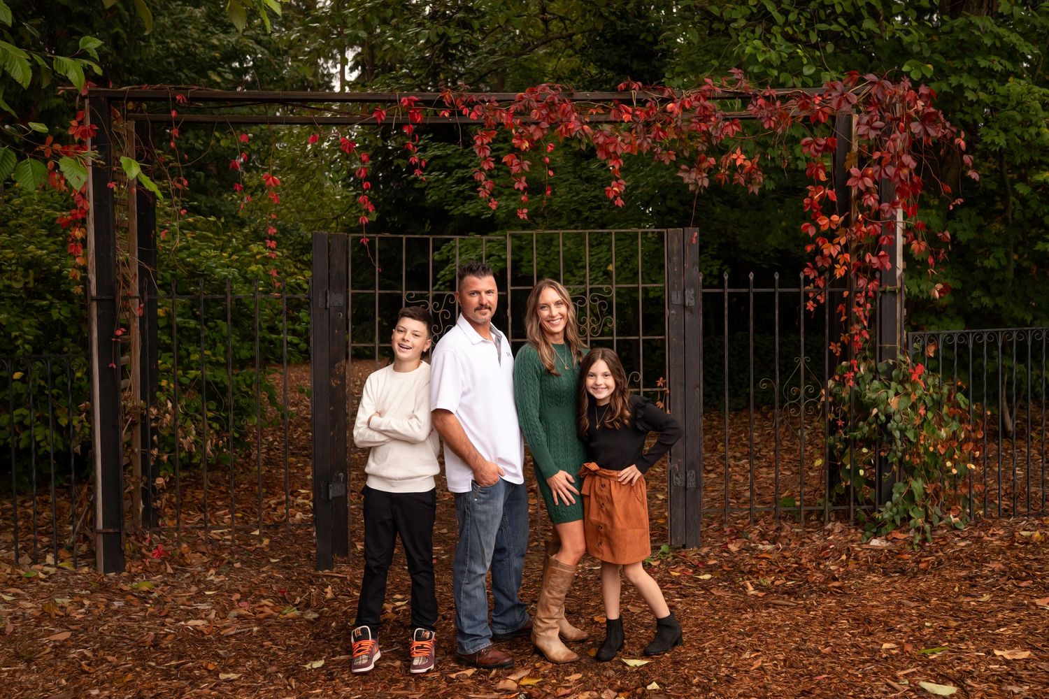 A group of people standing together in a garden setting with autumn foliage and red flowers in the background.