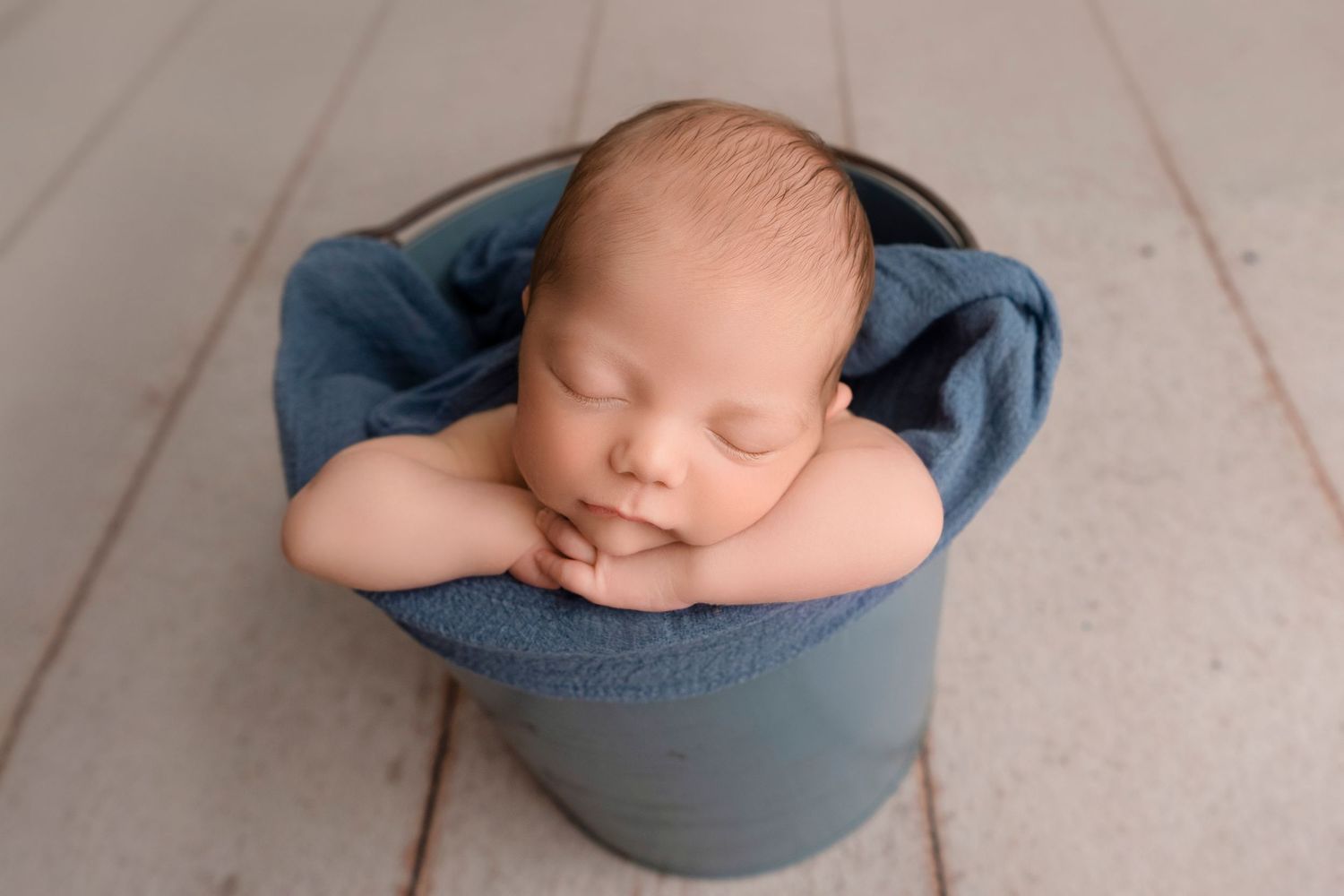 Newborn baby sleeping peacefully in a blue wrap on white textured background.