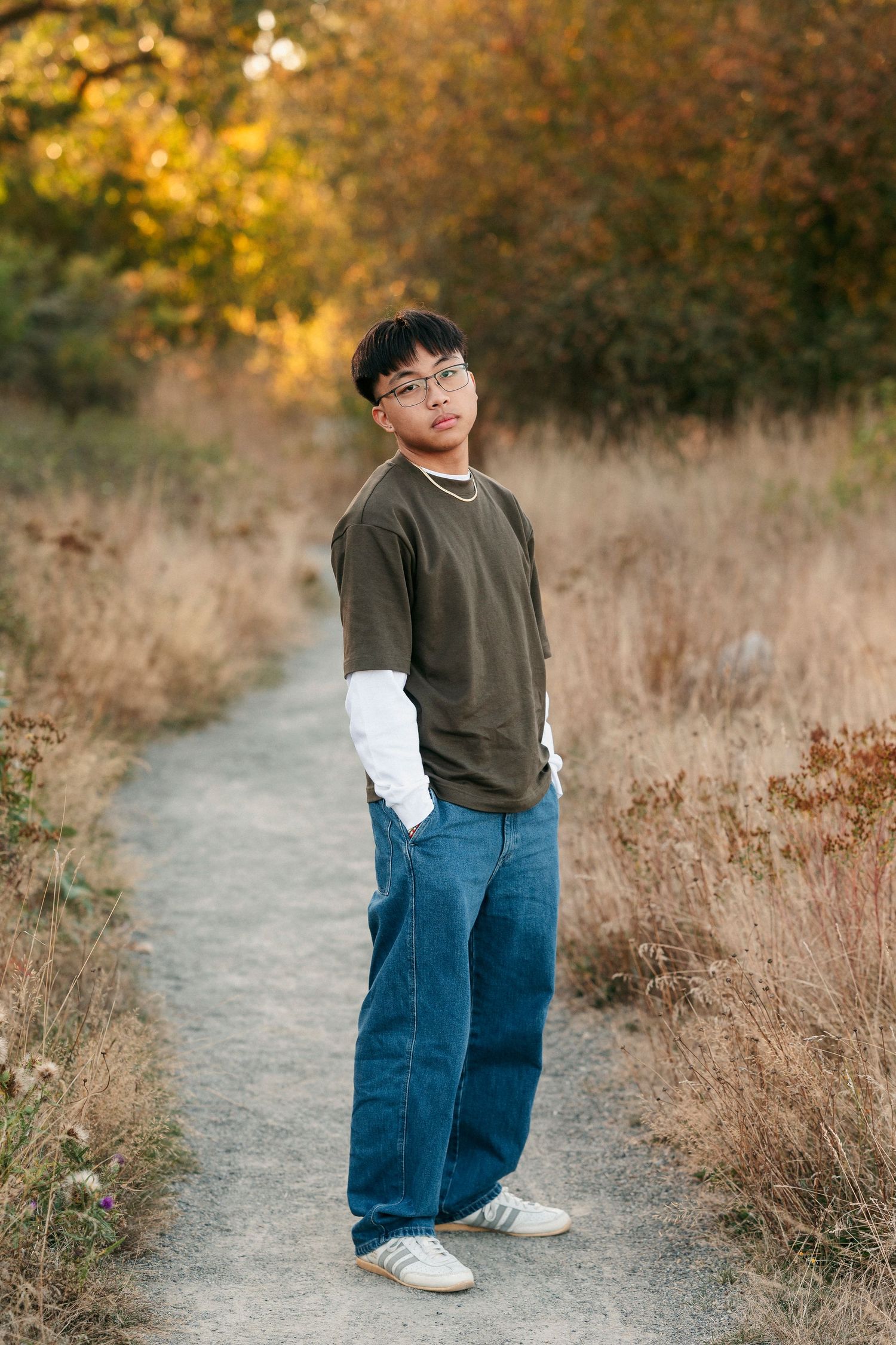 A person in casual attire walks along an autumn trail surrounded by golden dried grass and fall foliage.