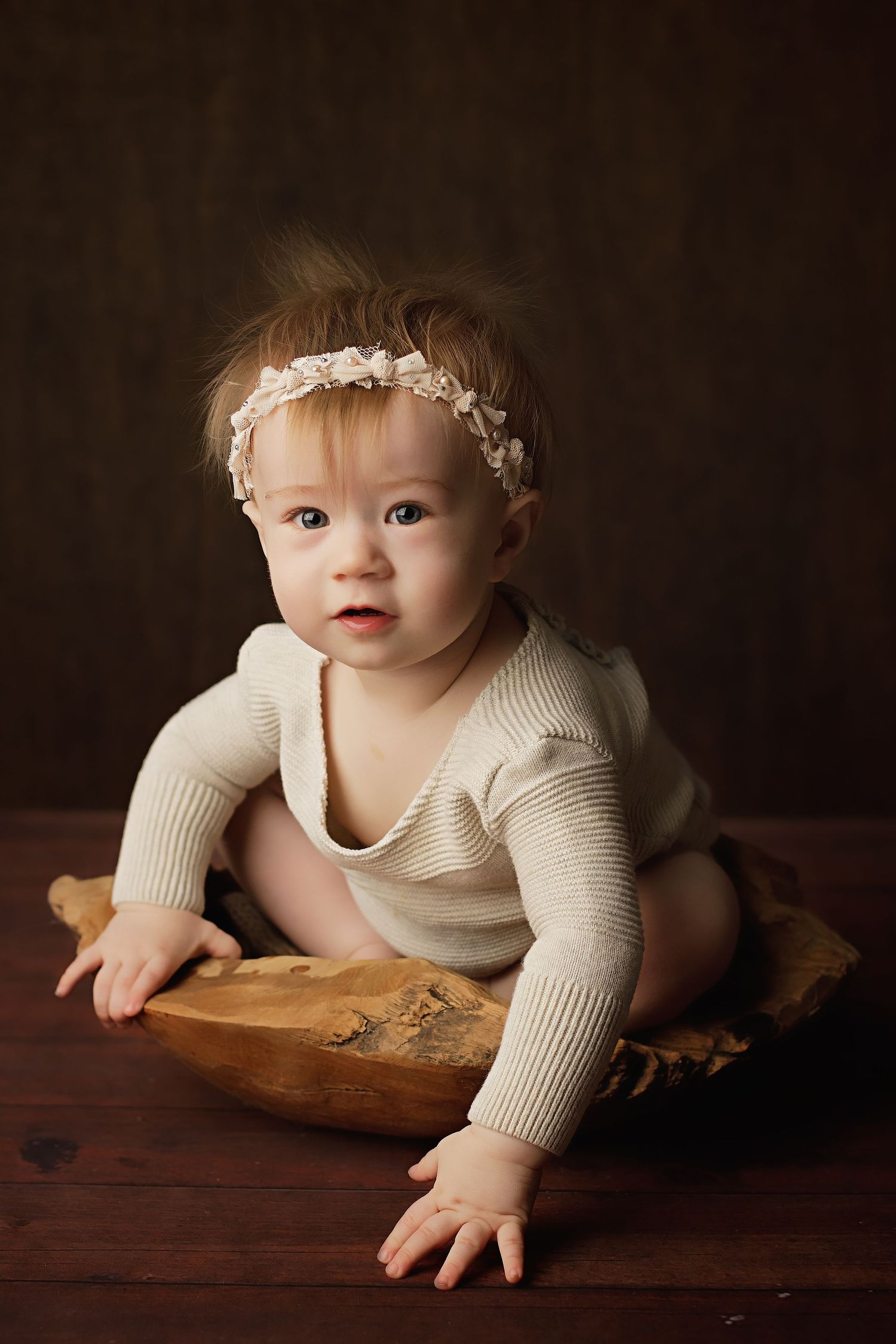 A baby in a cream sweater crawls across a wooden surface in a series of progressive motion shots against a dark background.