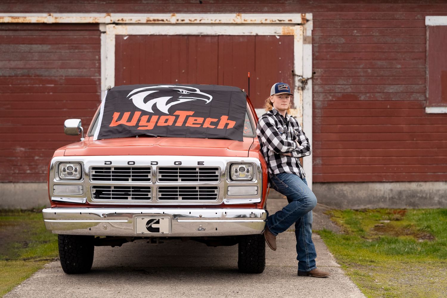 A vintage pickup truck parked in front of a rustic red barn wall.