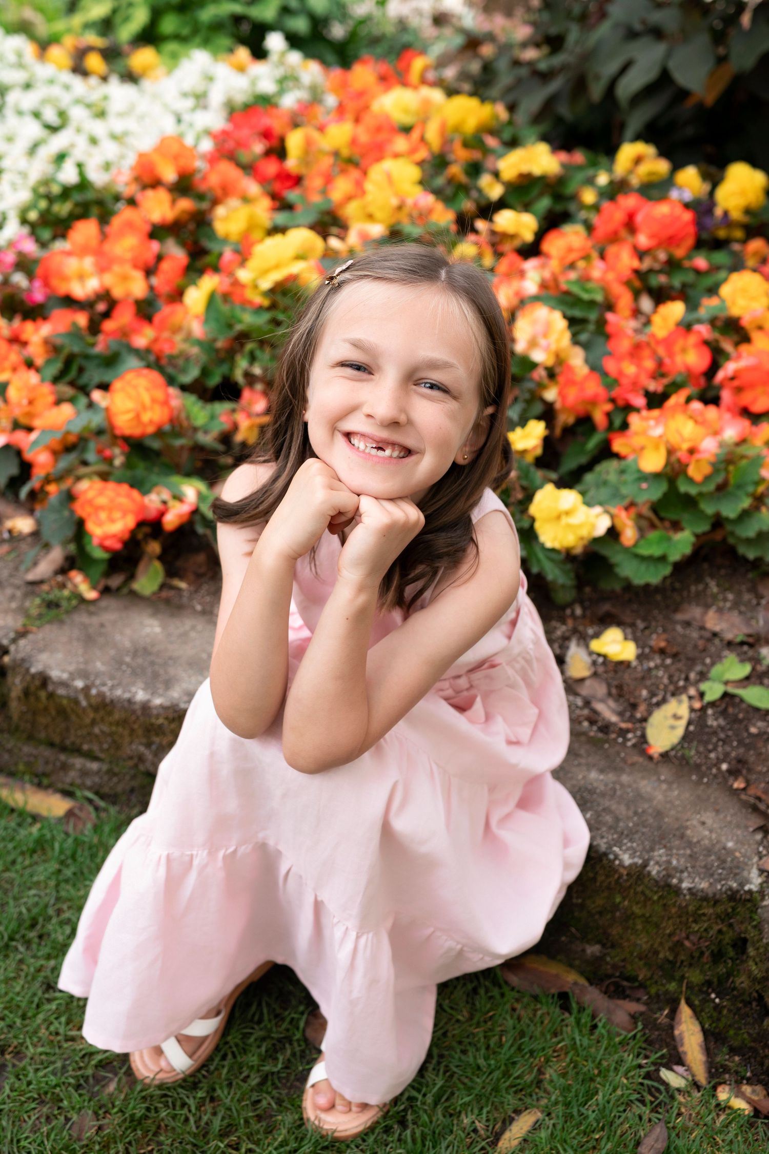 A child in a pink dress poses playfully among colorful flowers in a garden setting.