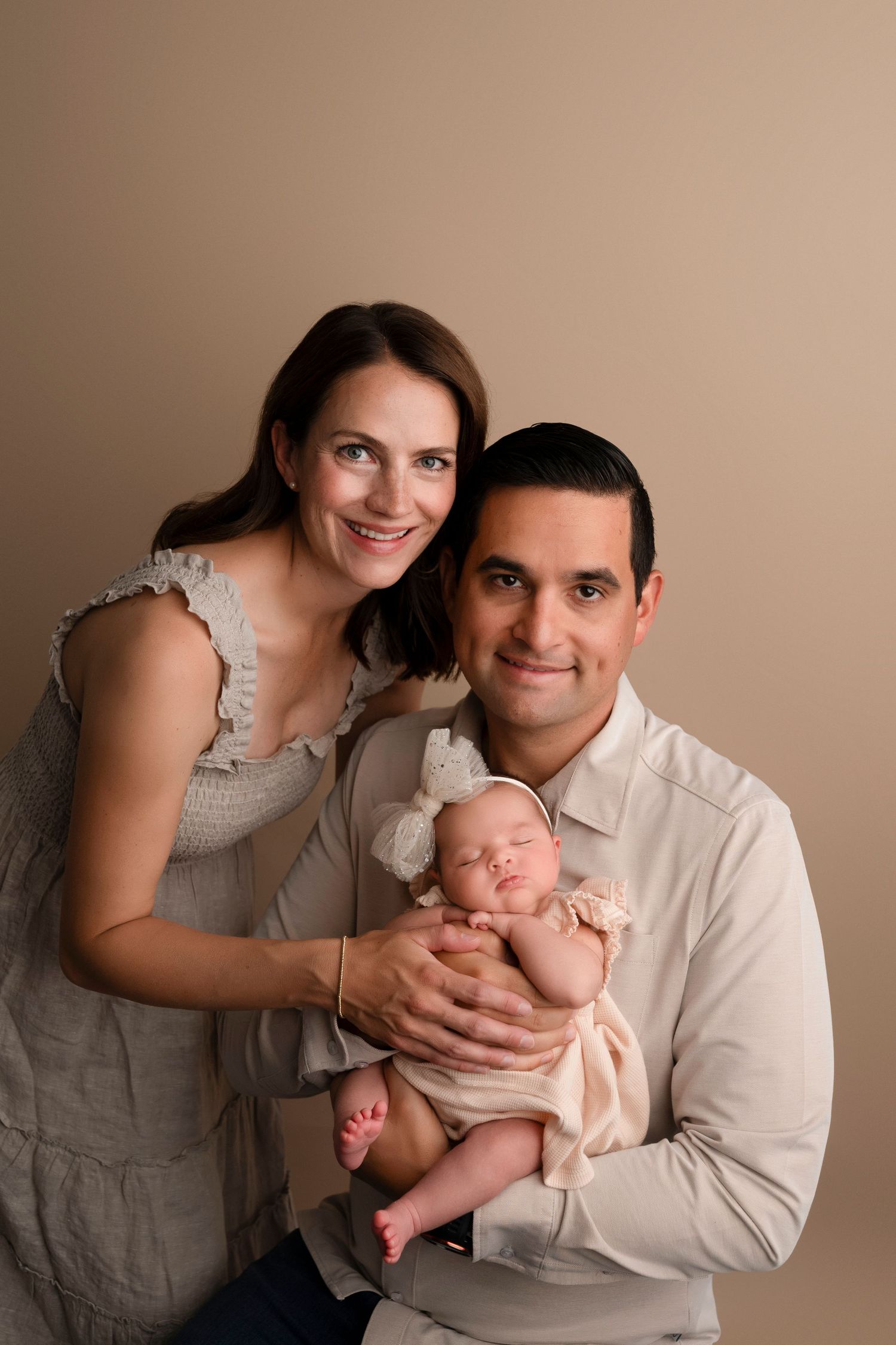A series of intimate family portraits showing parents with their newborn baby in soft, neutral studio lighting.