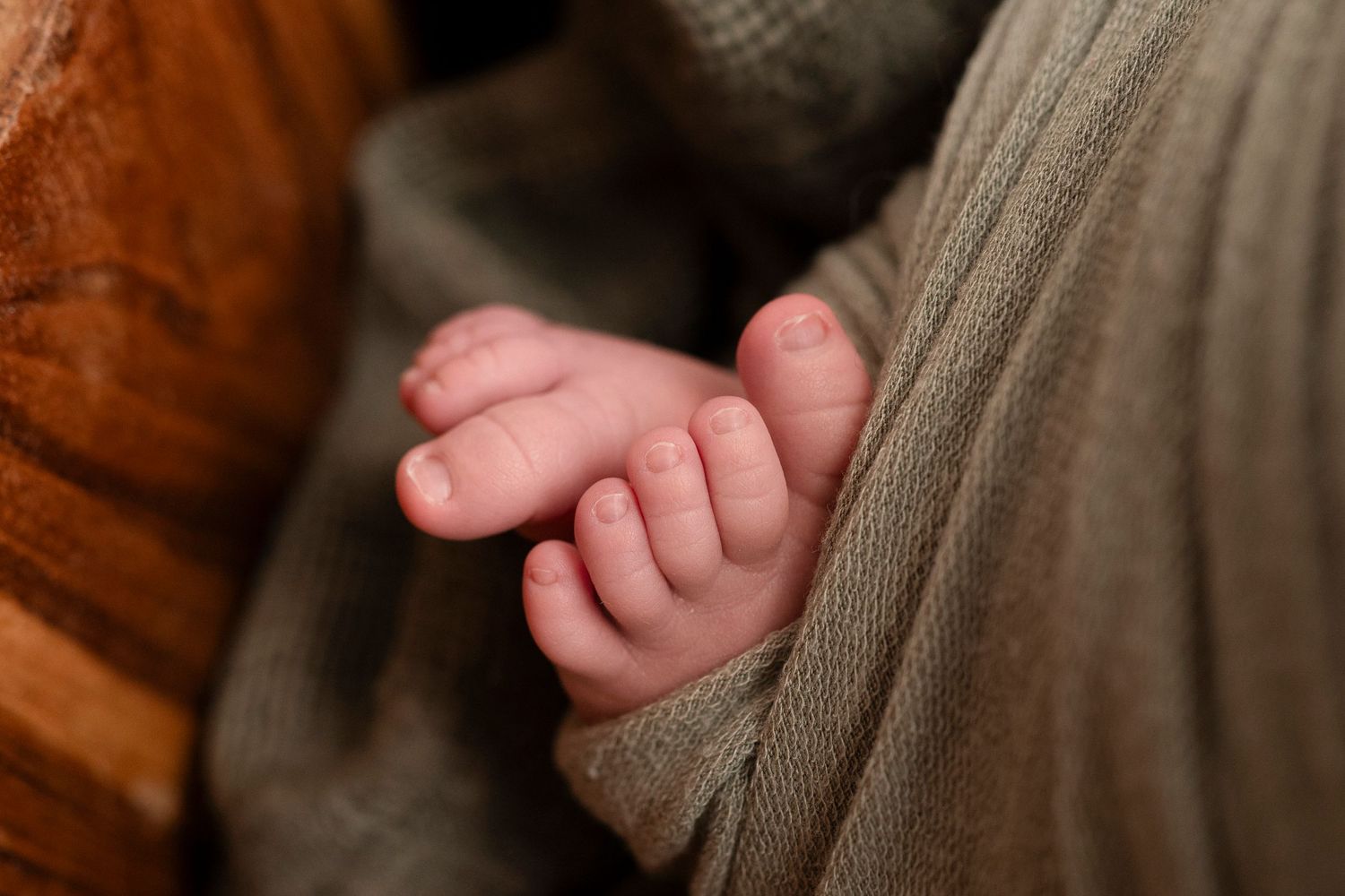 Tiny baby feet wearing knitted gray booties against a dark wooden background.
