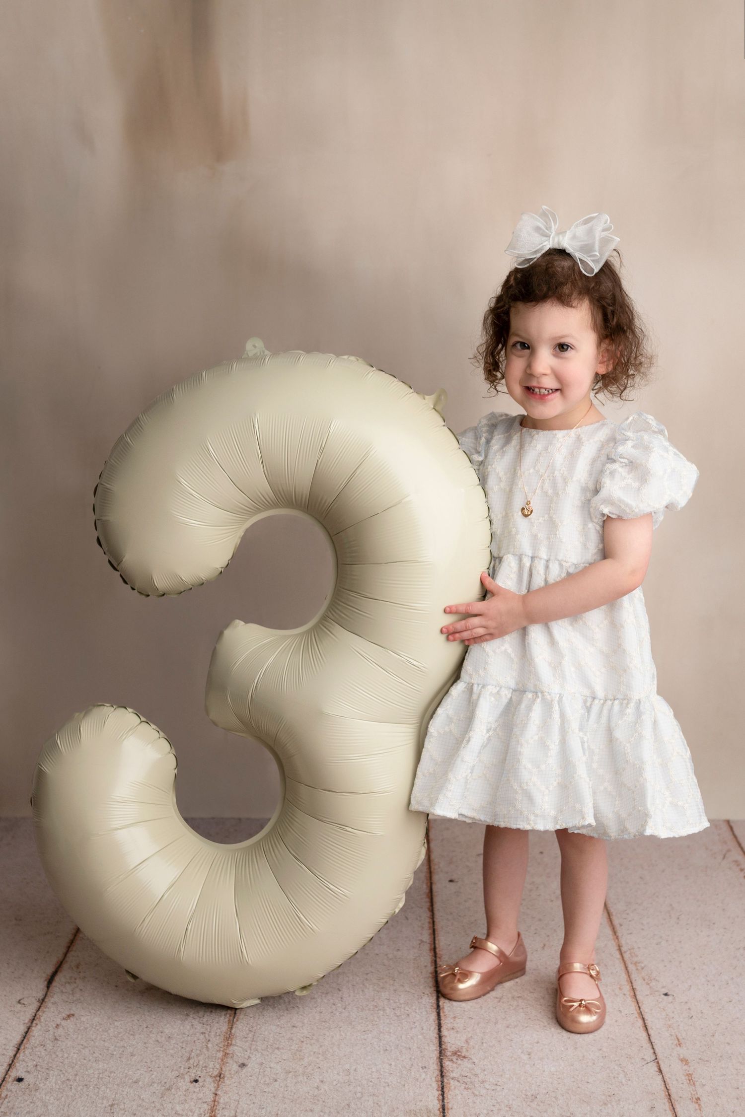A series of photos showing a child in a white dress posing with a large cream-colored circular cushion.