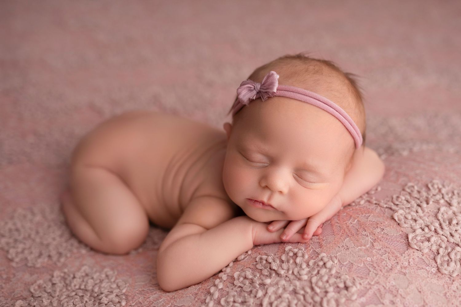 Sleeping newborn on pink textured blanket with delicate flower headband.