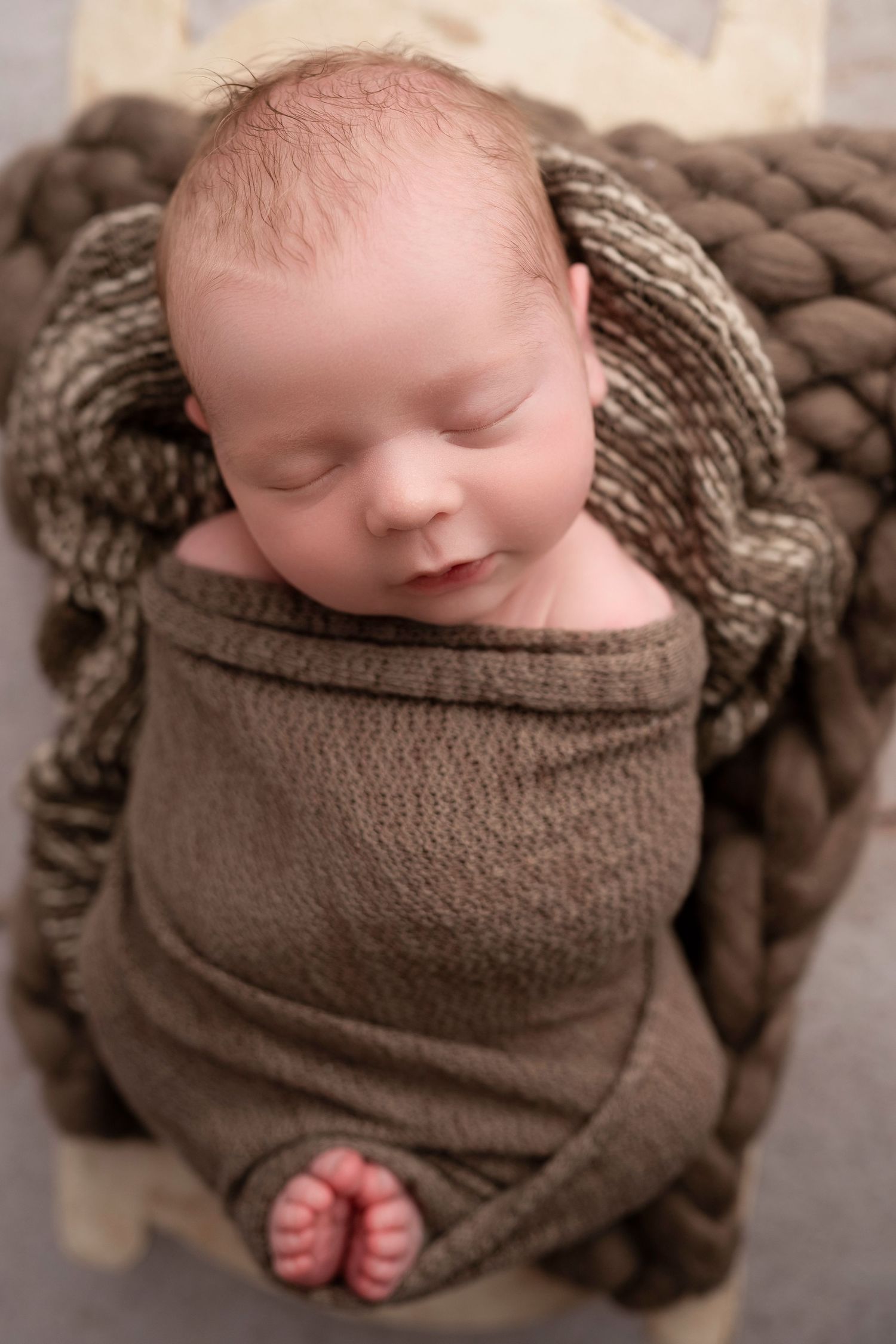 A sleeping newborn baby wrapped in a cozy brown knit blanket photographed from different angles.