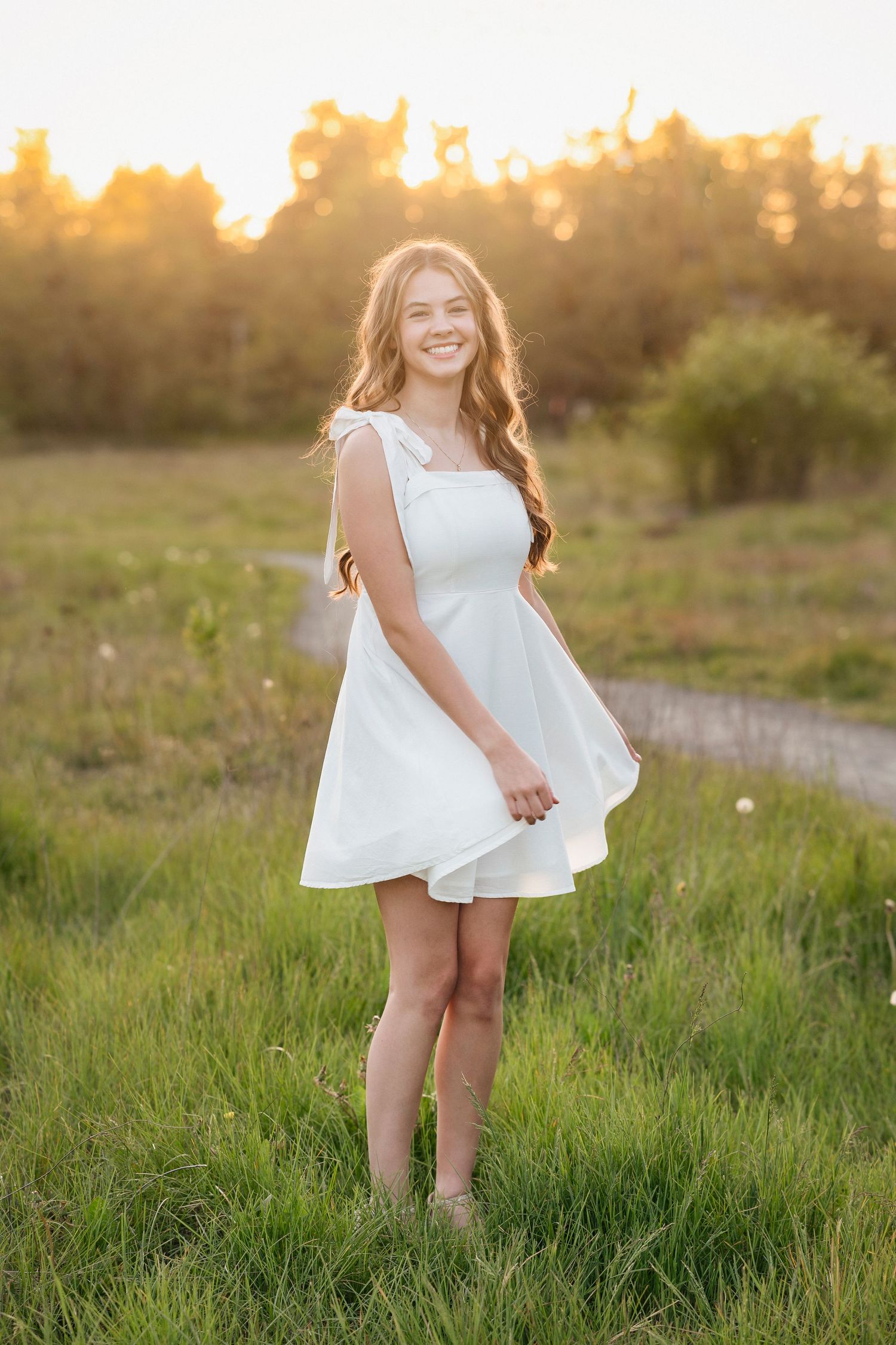 A white dress flows in the golden sunlight as someone walks through a grassy meadow at sunset.