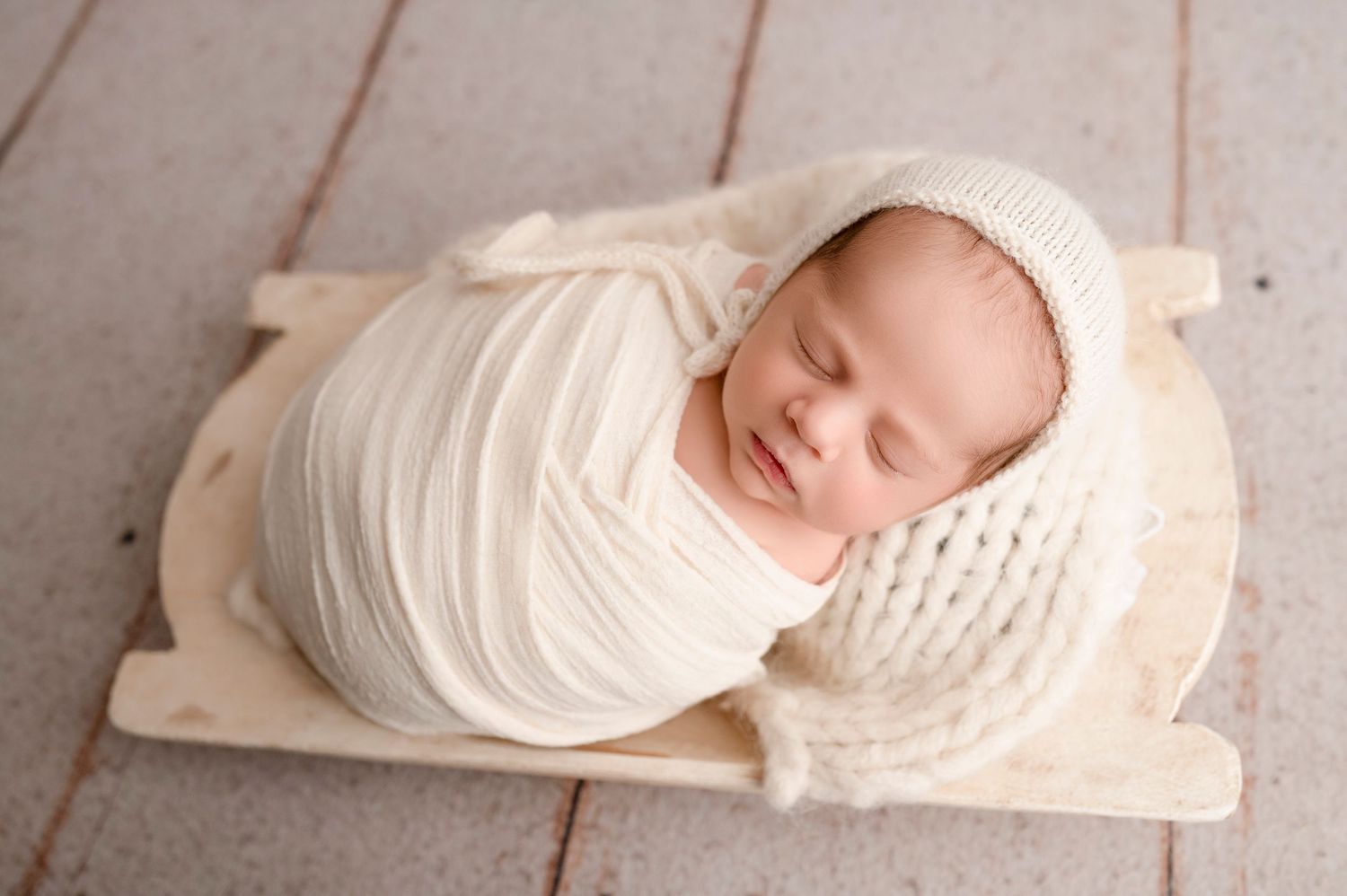 Tiny newborn swaddled in white fabric resting on textured wooden surface.