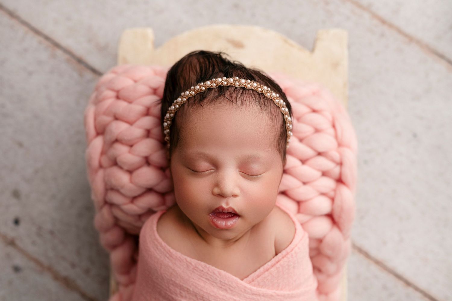 A sleeping newborn baby wrapped in soft pink knitted blanket rests peacefully during professional photography session.