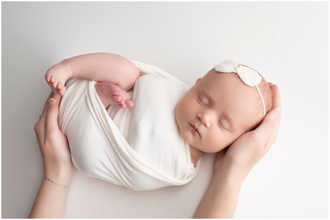 A series of minimalist newborn photography poses featuring a baby wrapped in soft white fabric against a light background.