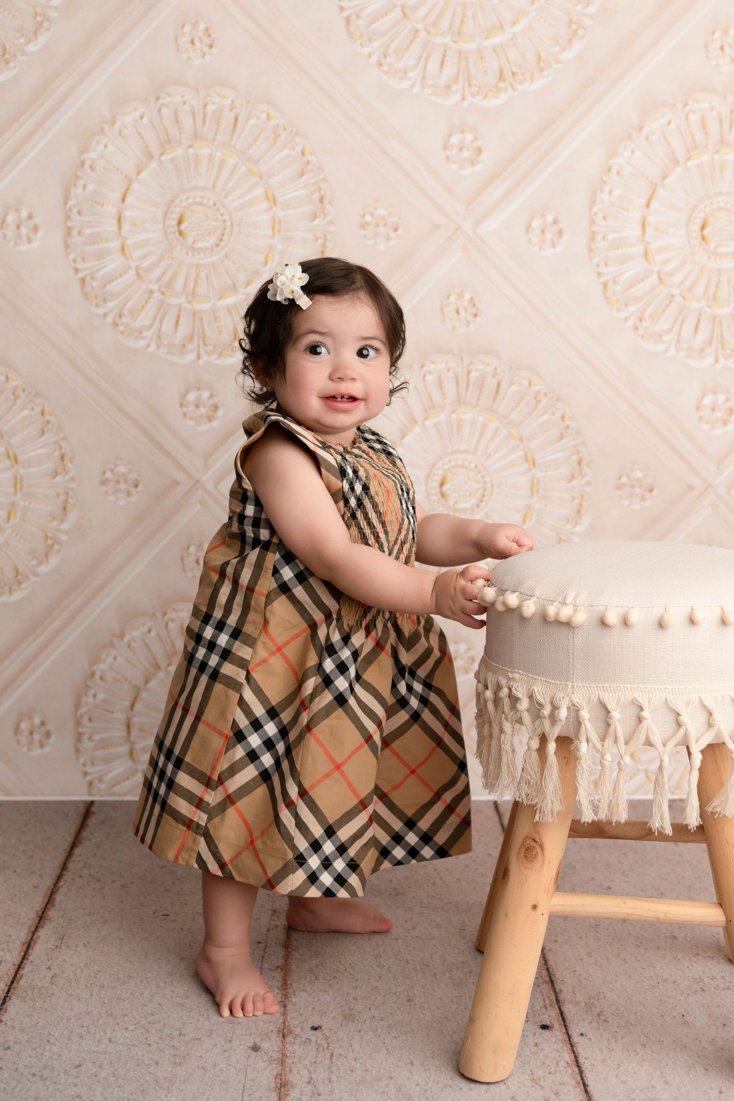 A small child in a plaid dress plays near a white decorative wall with vintage furniture.
